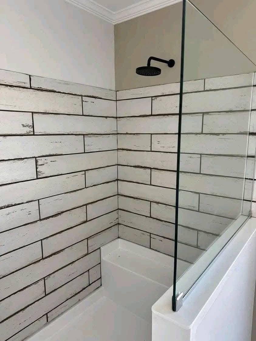 A modern shower area with weathered white subway tiles, a black showerhead, and a glass partition. The neutral tones feel calm and minimalistic.