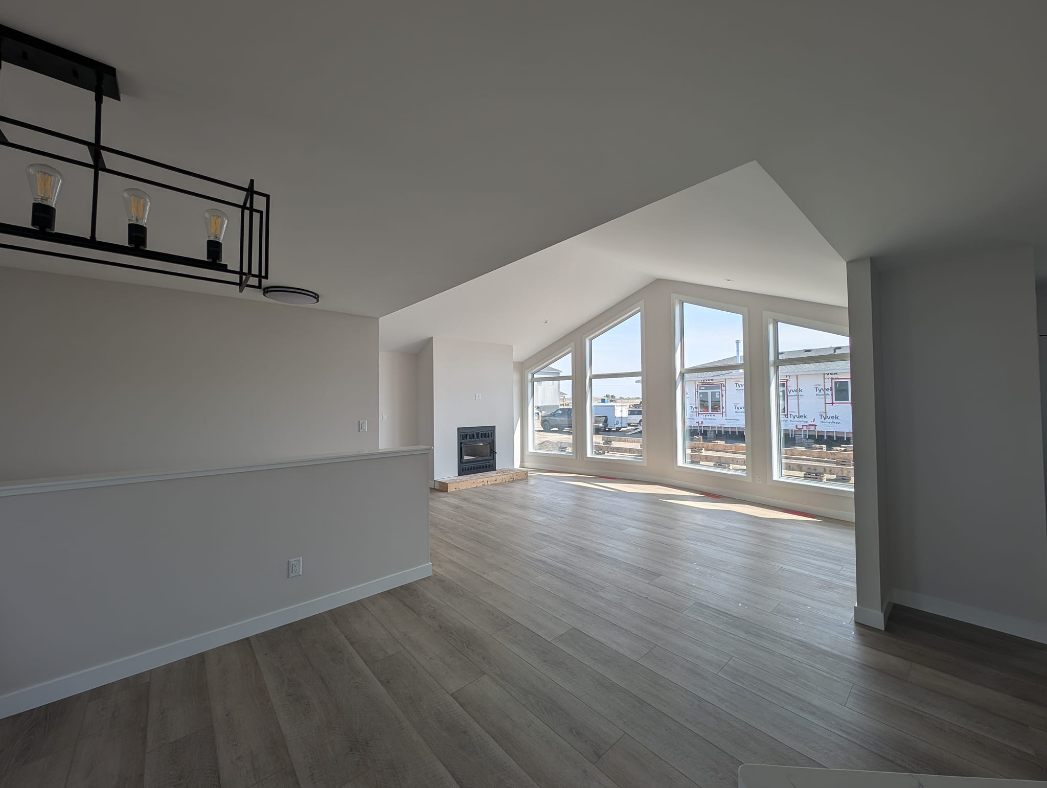 Spacious, modern living room with large windows, light wood flooring, a black metal chandelier, and a fireplace, conveying an airy, minimalist vibe.
