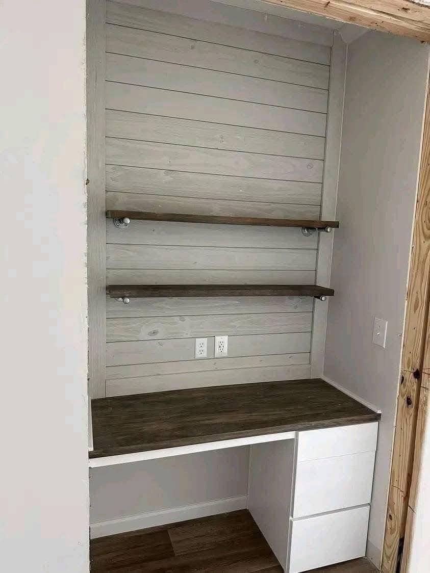 Small built-in office nook with two wooden shelves above a dark wood desk. Underneath, white drawers add storage. Light, neutral tones convey simplicity.