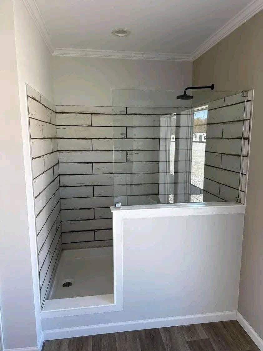 A modern bathroom features a small shower with rustic white wood panel walls, a partial glass enclosure, and a rain showerhead, creating a cozy, minimalist vibe.