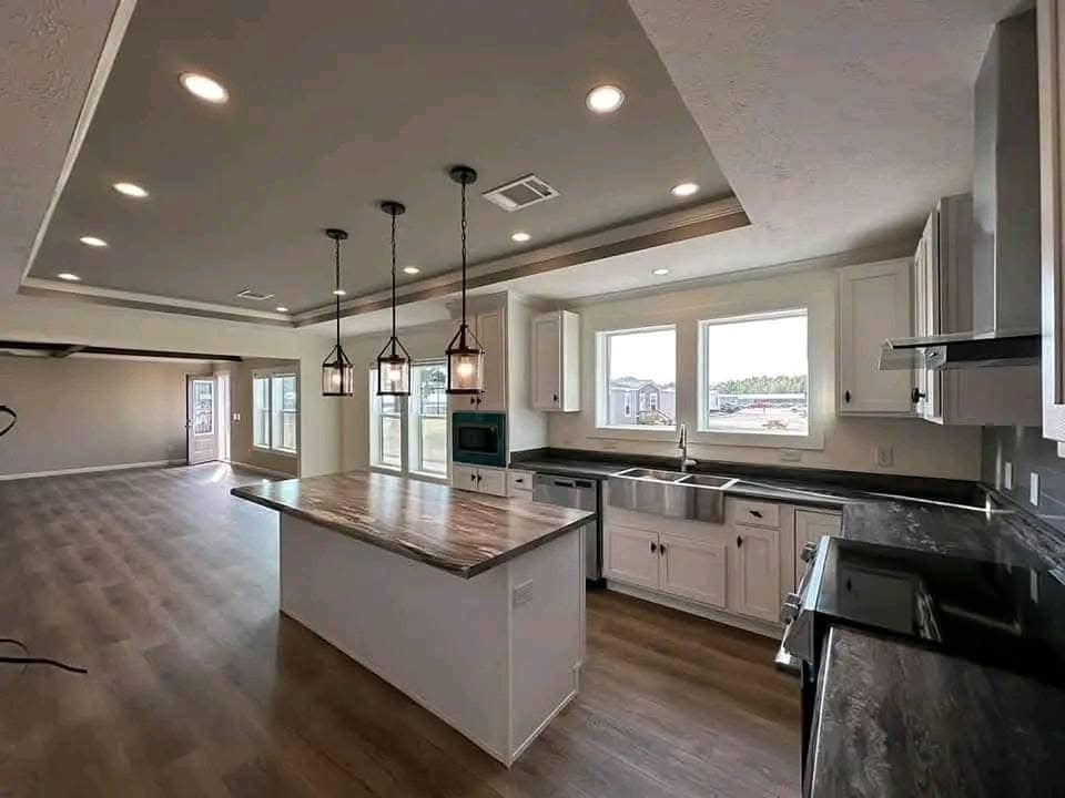 Modern kitchen with island, pendant lights, and hardwood floors. Large windows provide natural light, creating an open and inviting atmosphere.
