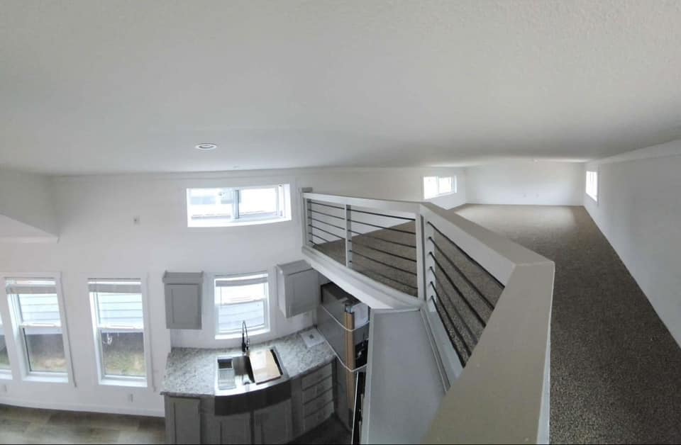 View of a modern loft-style apartment with large windows, a compact kitchen with granite countertops, and an open mezzanine overlooking the space.