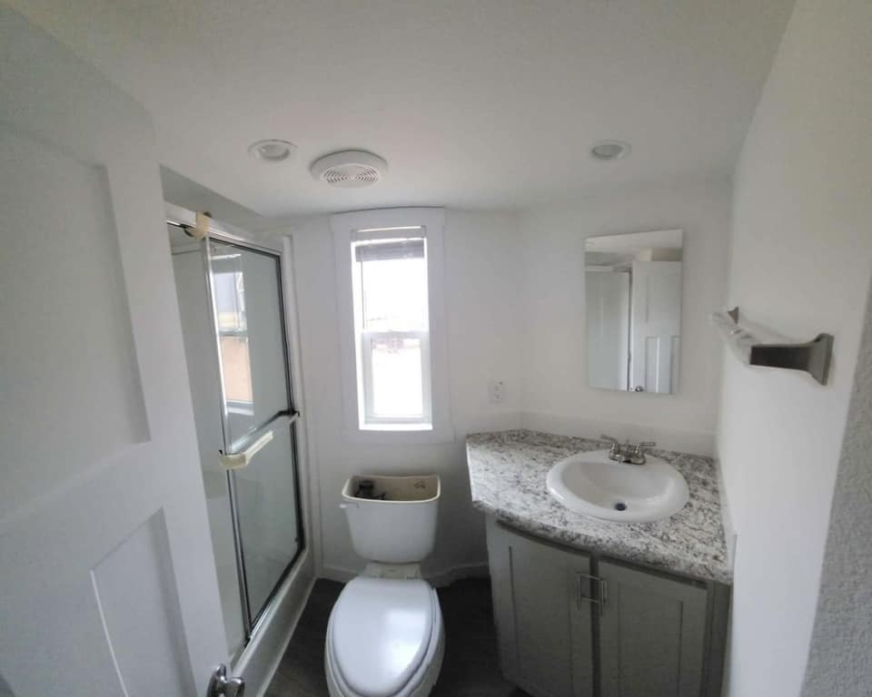 Small bathroom with a window, glass shower door, and modern vanity. Neutral tones and natural light create a clean, minimalist feel.
