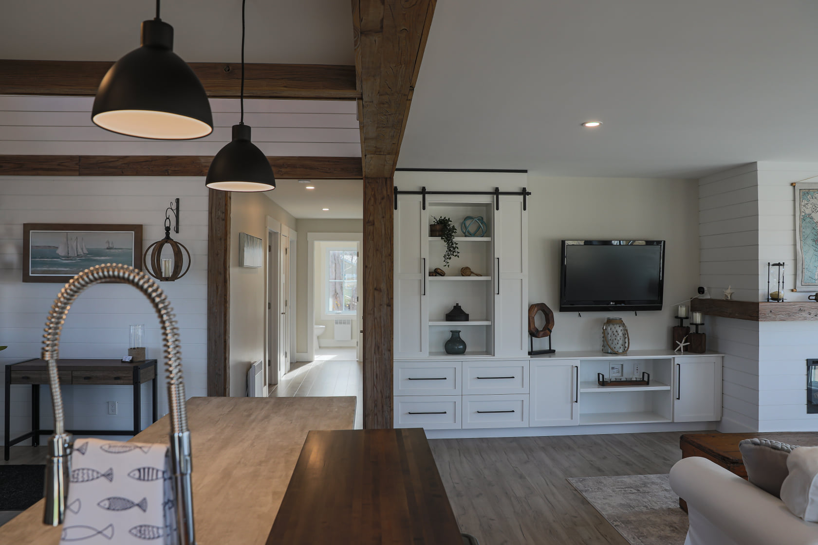 Modern living room with wooden beams and a farmhouse style. A built-in entertainment center features a TV, shelves, and a sliding barn door. Cozy and inviting atmosphere.