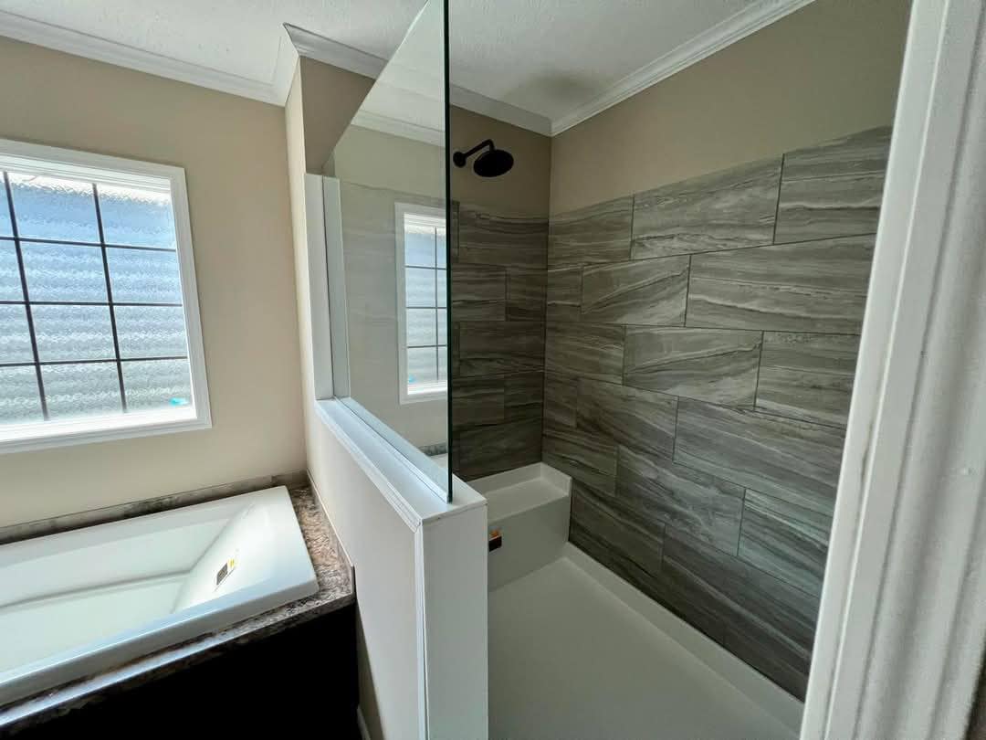 Modern bathroom with a tiled shower, glass partition, and adjacent bathtub. Natural light from a window creates a serene, clean ambiance.