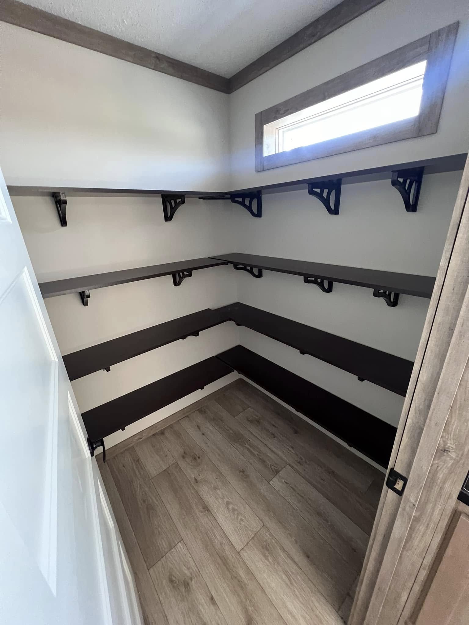 Modern kitchen with sleek black marble countertops, stainless steel appliances, light wood flooring, and a white brick accent wall, creating an elegant, airy feel.