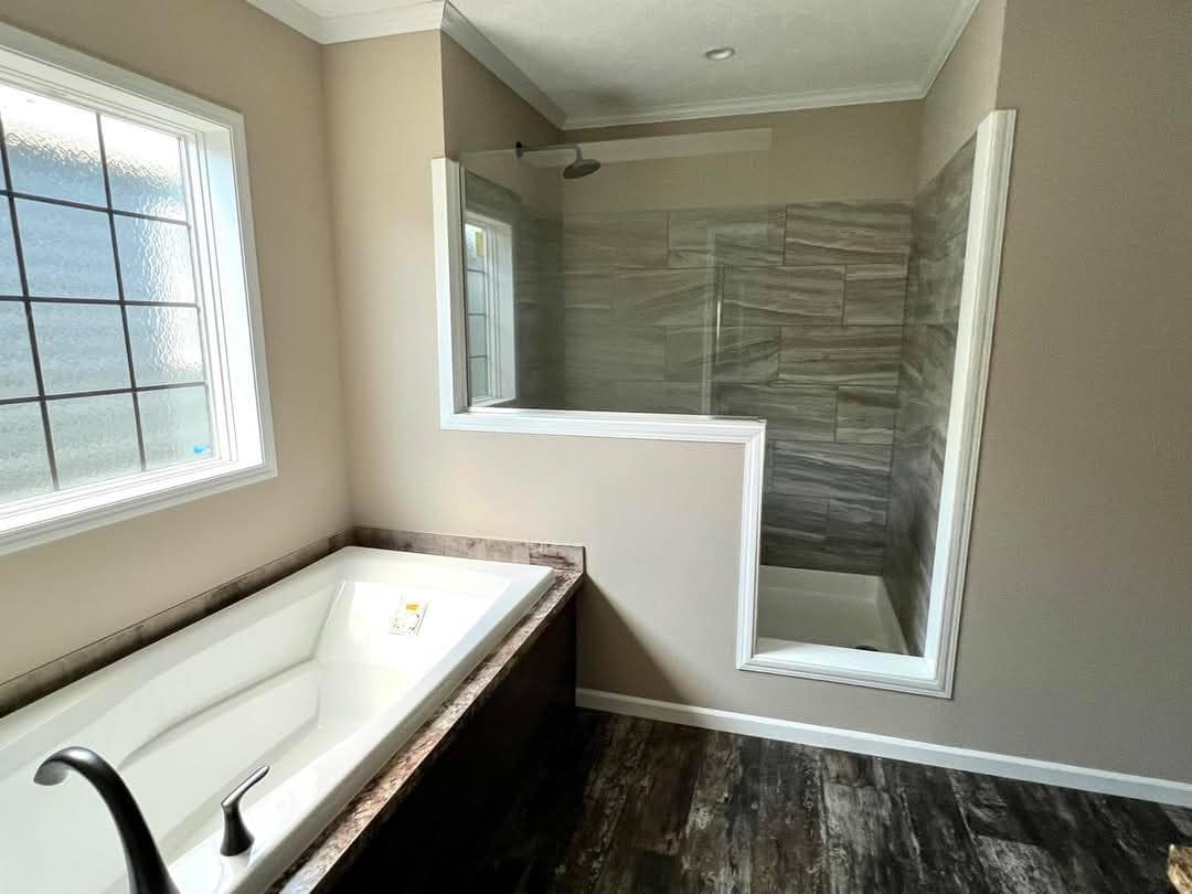 Modern bathroom with a white bathtub and a glass-enclosed shower. Natural light filters through a grid-patterned window, creating a calm, clean ambiance.