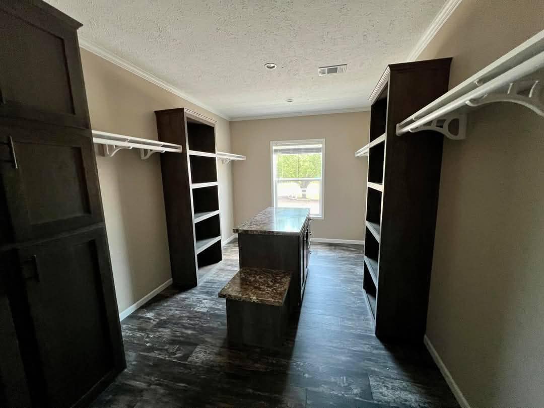 Spacious walk-in closet with dark wood shelves, a marble-topped island, and a large window. Light walls and ceiling create an airy, organized feel.