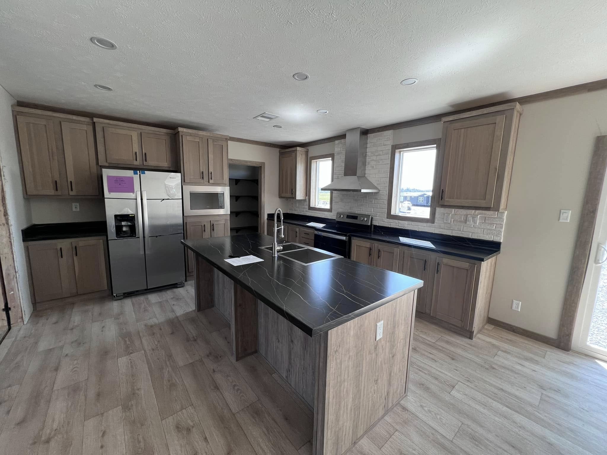 Spacious kitchen with wooden cabinets, black countertops, and a central island. Stainless steel appliances and ample natural light create a modern feel.
