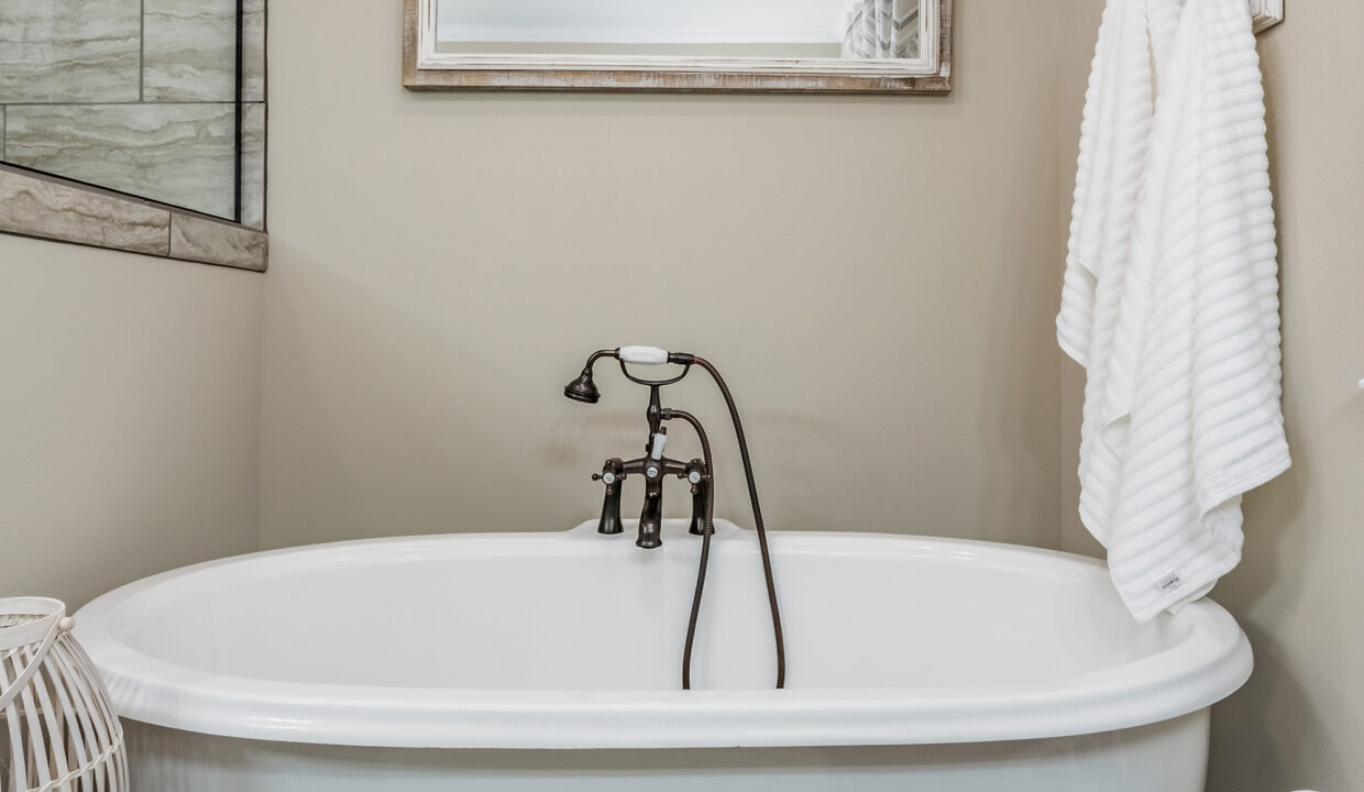 A white, freestanding bathtub with vintage-style black faucets sits against a beige wall. A white towel hangs next to it, creating a serene, relaxing vibe.