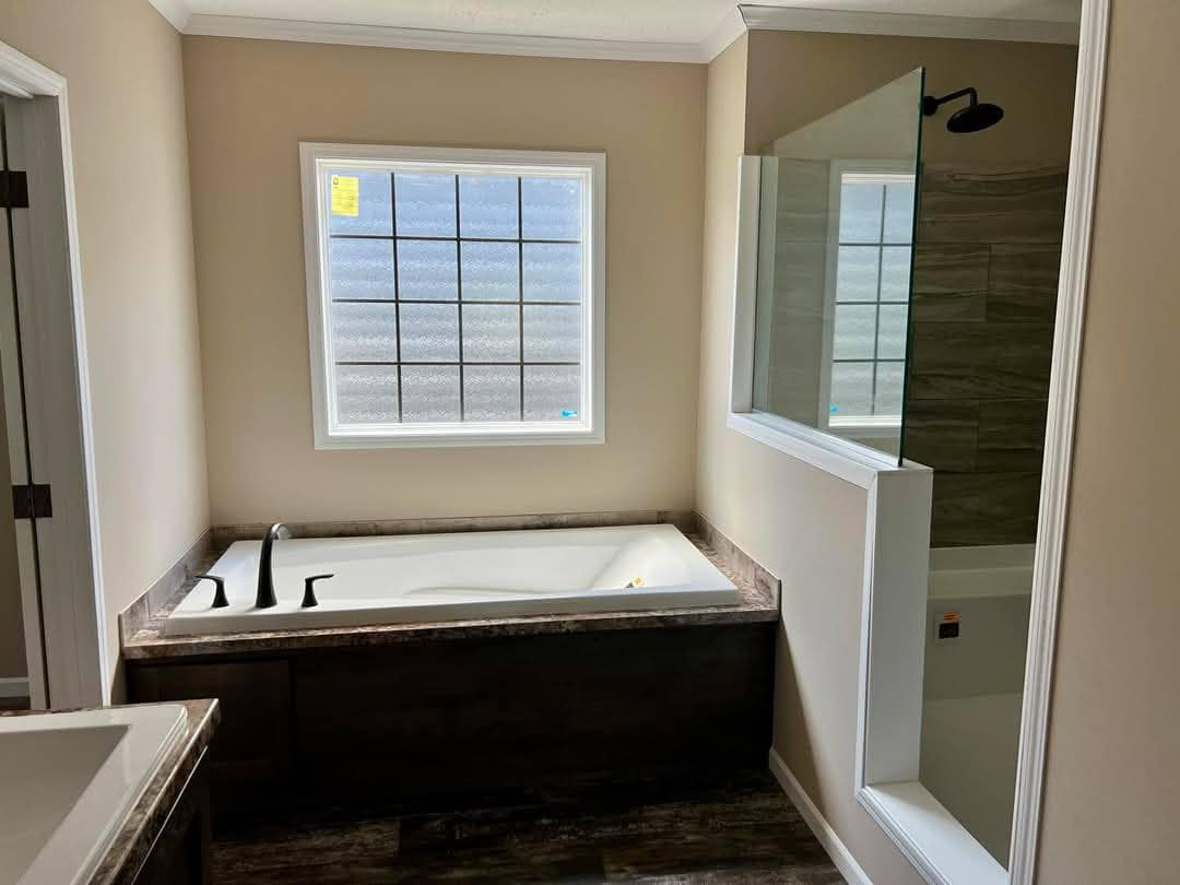 Modern bathroom with a rectangular bathtub under a frosted window, adjacent to a glass-enclosed shower. Neutral tones create a calm, inviting atmosphere.
