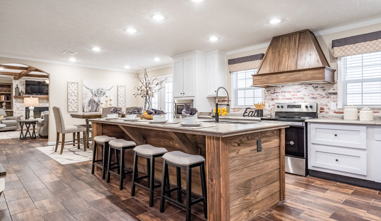 Modern, cozy living room with a fireplace, beige walls, and wood flooring. Patterned armchairs face a beige sofa. An open kitchen is visible in the background.