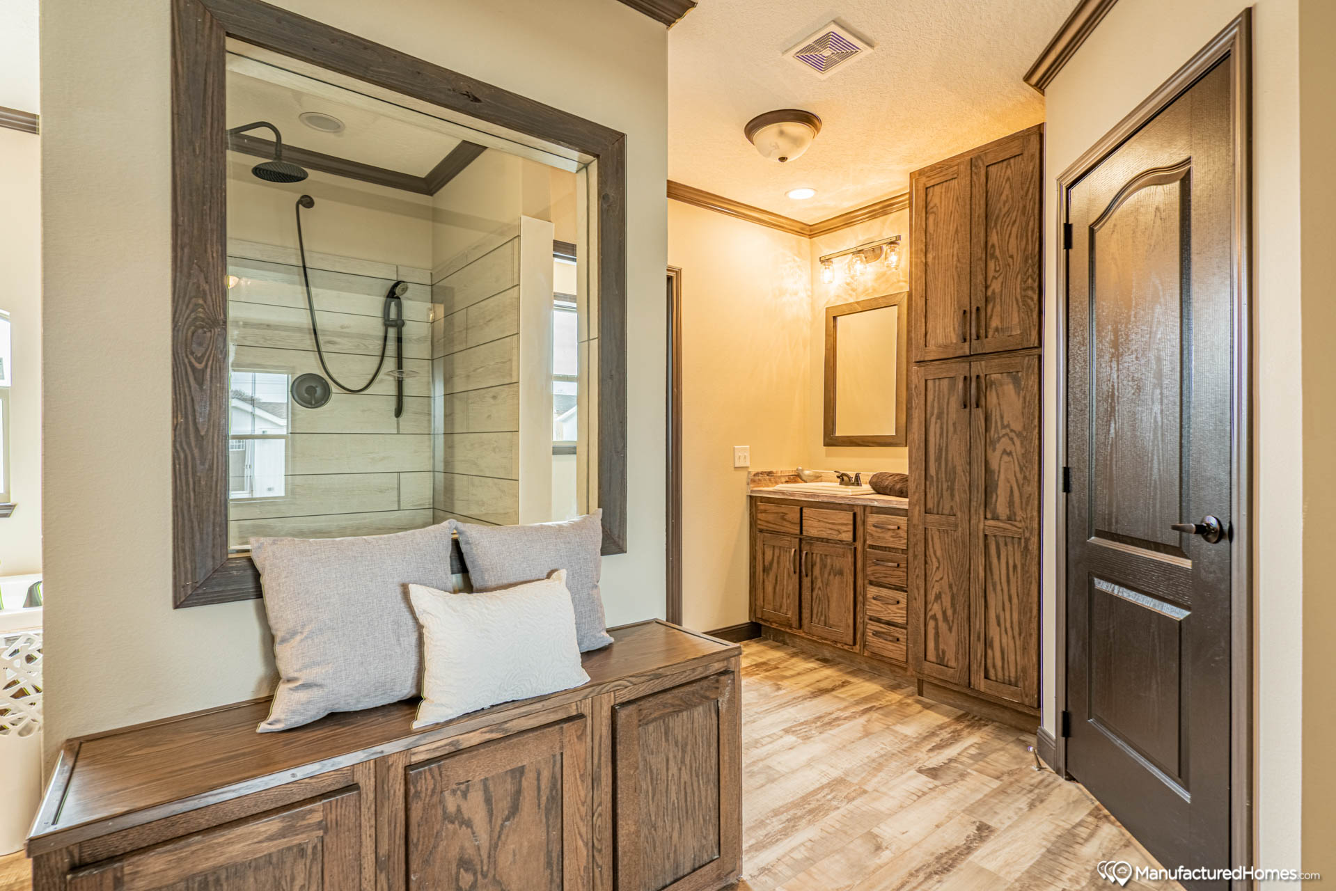 Cozy bathroom with wooden cabinets and beige walls. A large mirror reflects a modern shower with a rainfall showerhead. Soft lighting creates a warm atmosphere.