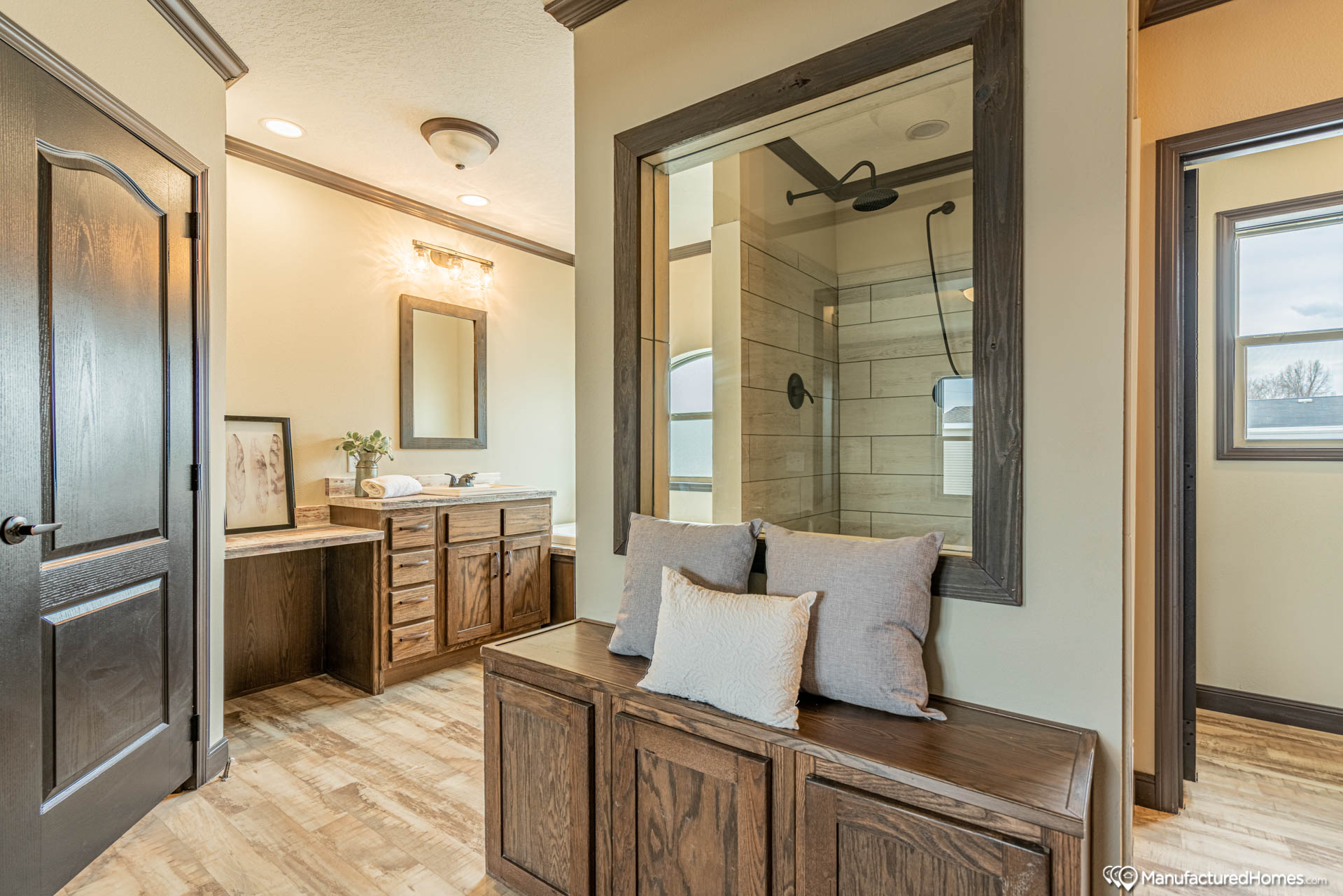 Bright bathroom with wood accents and a cozy bench with cushions. Features a modern vanity, large mirror, and glass-enclosed shower. Warm, inviting atmosphere.