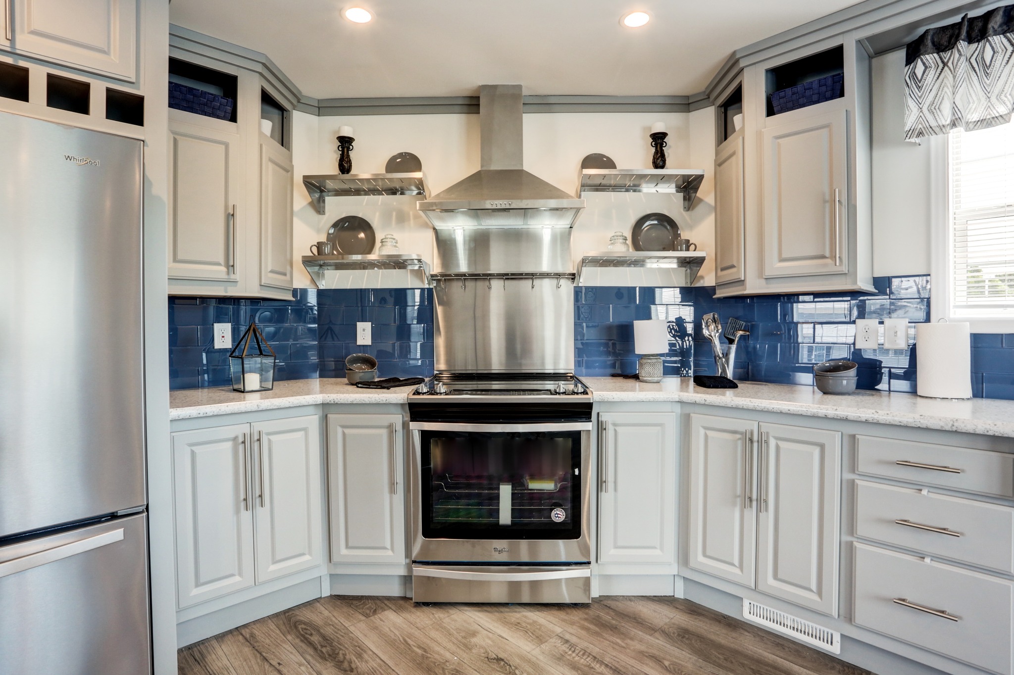 Modern kitchen with stainless steel appliances, light gray cabinets, and blue tile backsplash. Shelves hold dishes, creating a clean, stylish look.