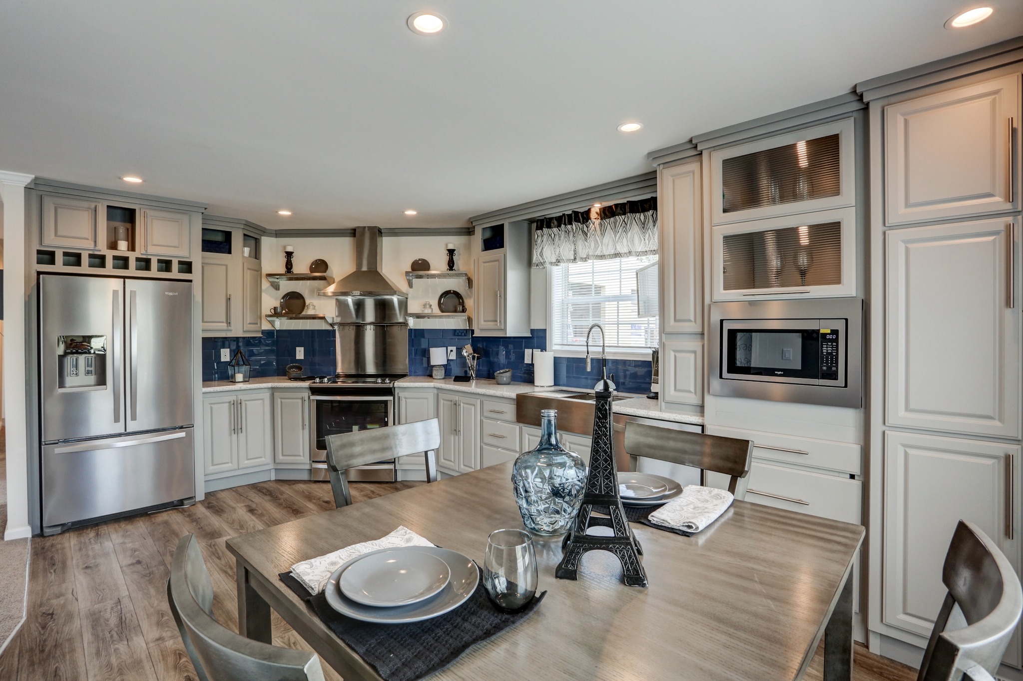 Modern kitchen with cream cabinets, stainless steel appliances, and blue backsplash. A wooden table is set with plates and an Eiffel Tower centerpiece.