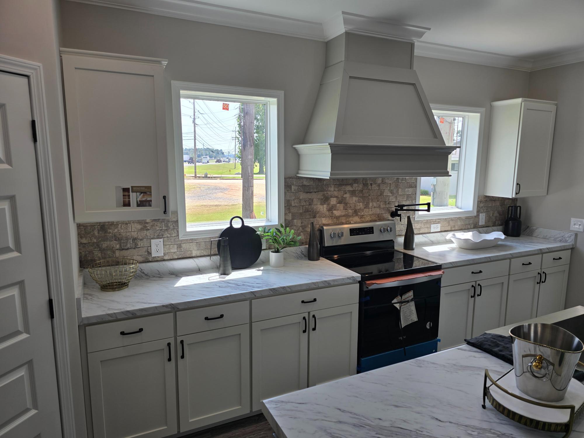 Spacious modern kitchen with white cabinets, marble countertops, and three pendant lights. Central island set with plates and cups. Bright natural light from windows.