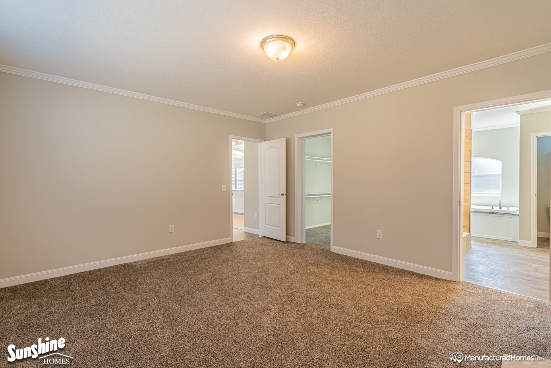 A spacious, empty room with beige walls and carpet. Two doors lead to a closet and a bathroom. Soft lighting creates a warm, inviting atmosphere.