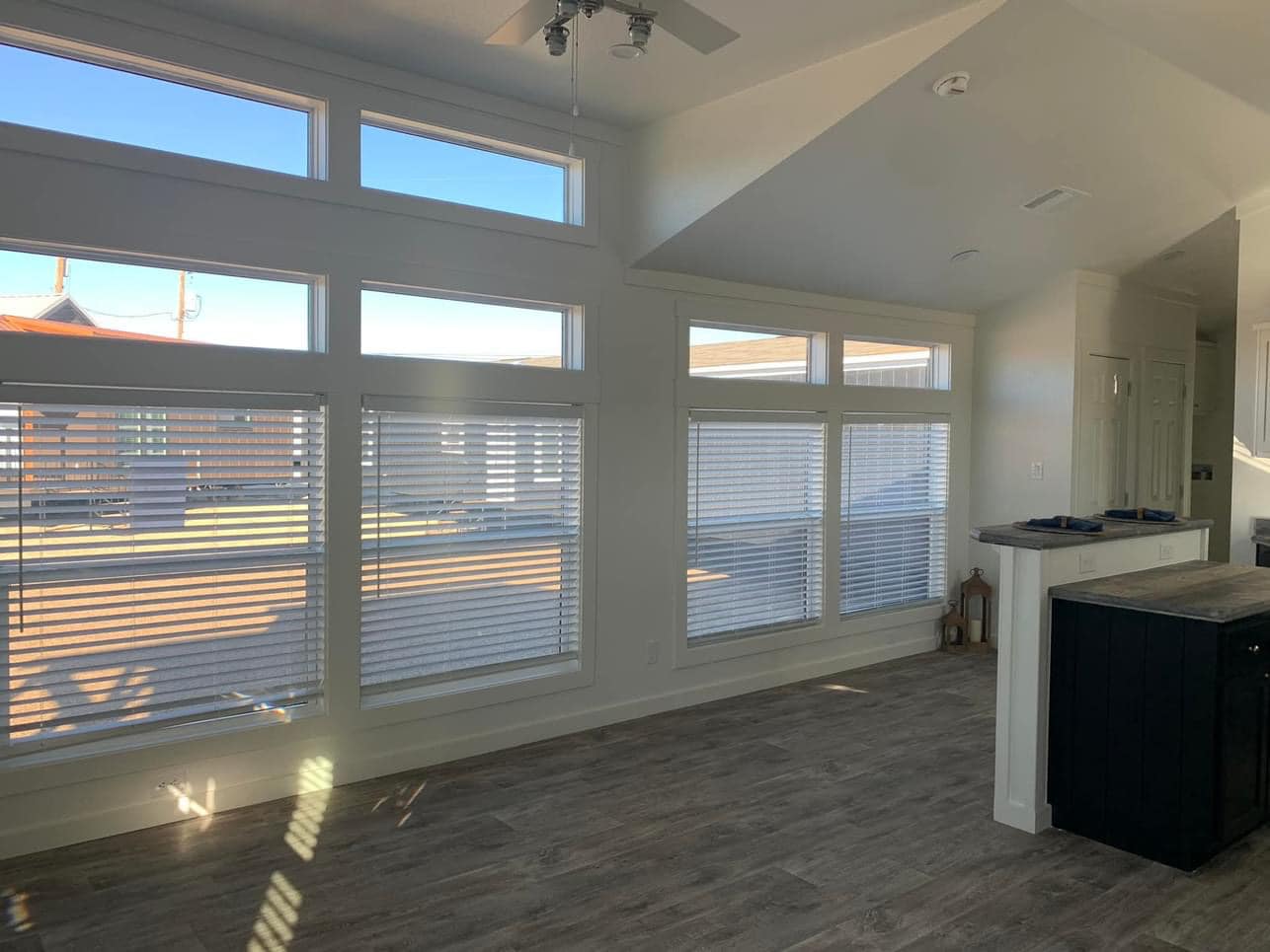 Bright, modern living room with large windows, light-colored walls, and wooden flooring. A vaulted ceiling adds an open, airy feel.