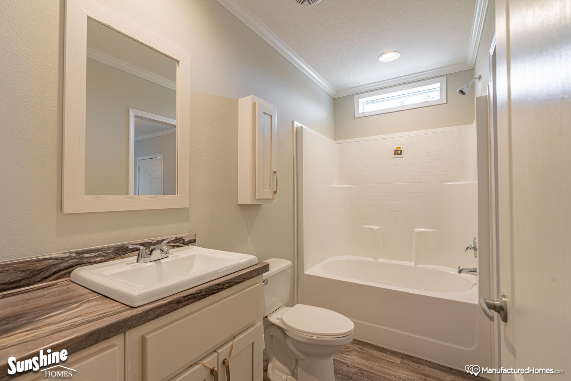 Bright bathroom with a white bathtub, sink, and toilet. Wooden vanity with a mirror above. Natural light from a small window. Clean and modern.