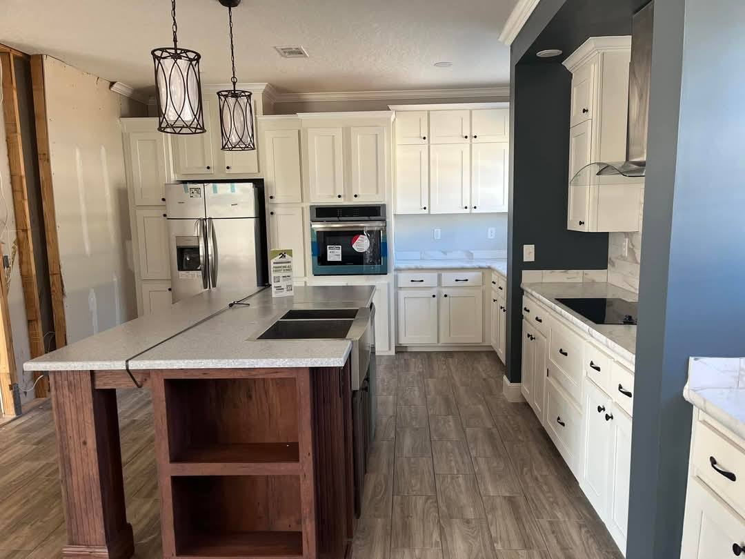 Modern kitchen with dark wood island, marble countertops, and white cabinets. Stainless steel appliances, wood flooring, and pendant lights create a warm ambiance.