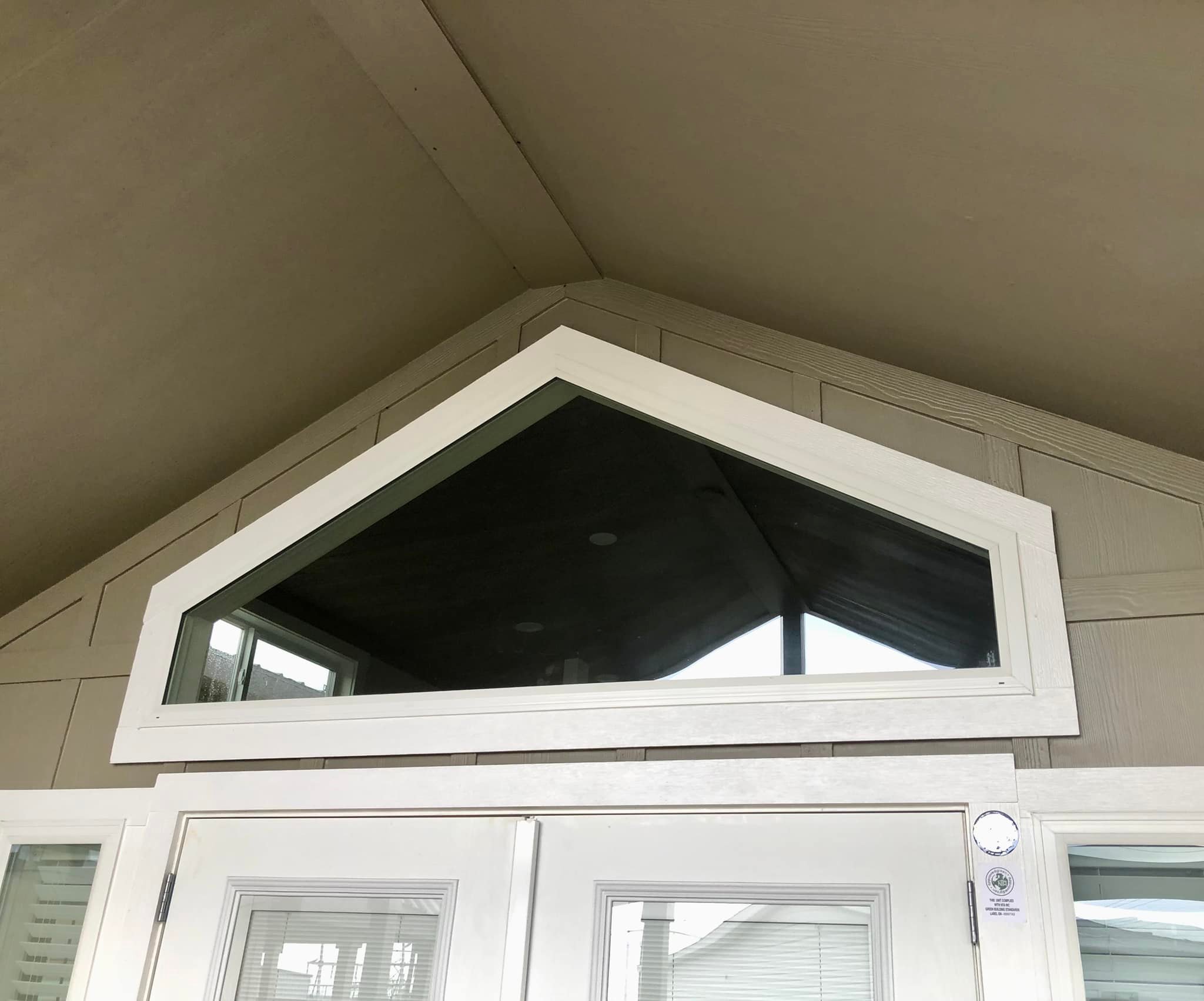 A white French door with blinds on a covered porch, next to a modern outdoor lantern on beige siding. The scene is calm and inviting.