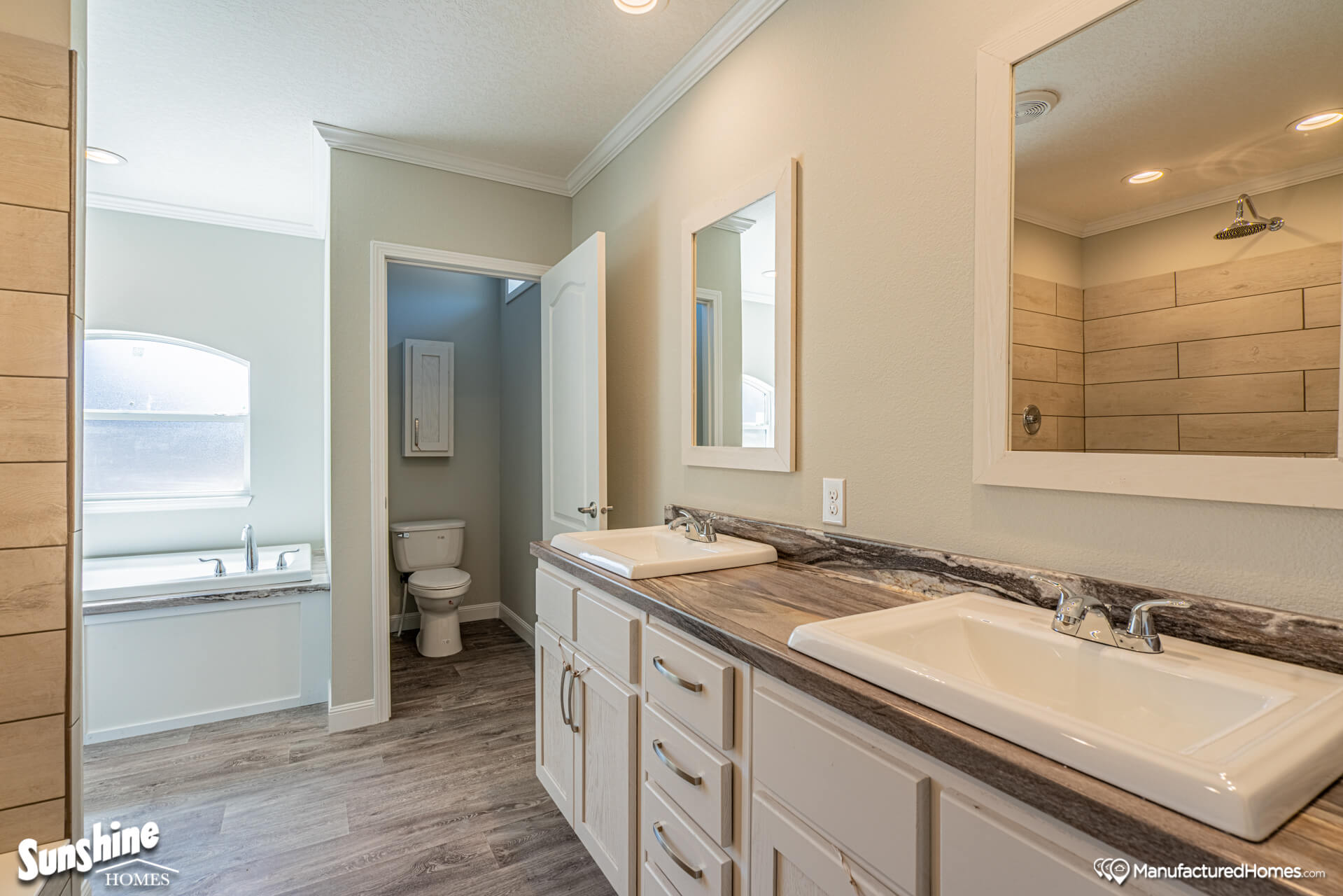 Bright, modern bathroom with dual sinks on a wooden counter, two mirrors, a walk-in shower with wood-pattern tiles, and a separate bathtub by an arched window.