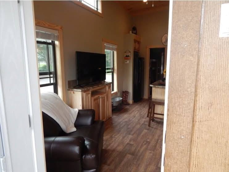 Compact, cozy living space with wood-paneled walls and floor. Features a leather chair, TV on a stand, kitchen area with a stool. Warm, inviting ambiance.