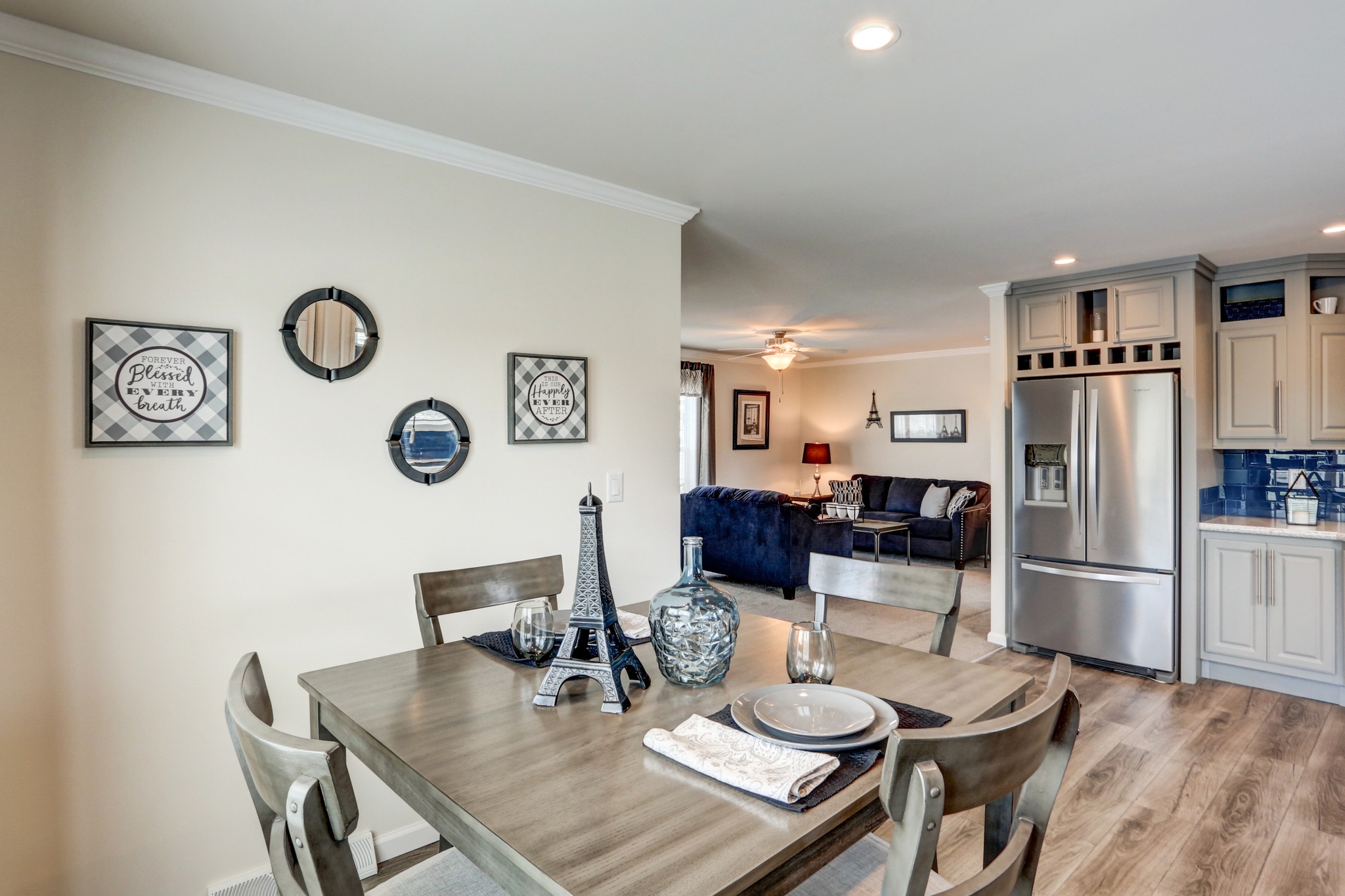 Dining room with a wooden table set for two, Eiffel Tower centerpiece. Open-plan layout reveals a cozy living space and modern kitchen. Warm, welcoming atmosphere.