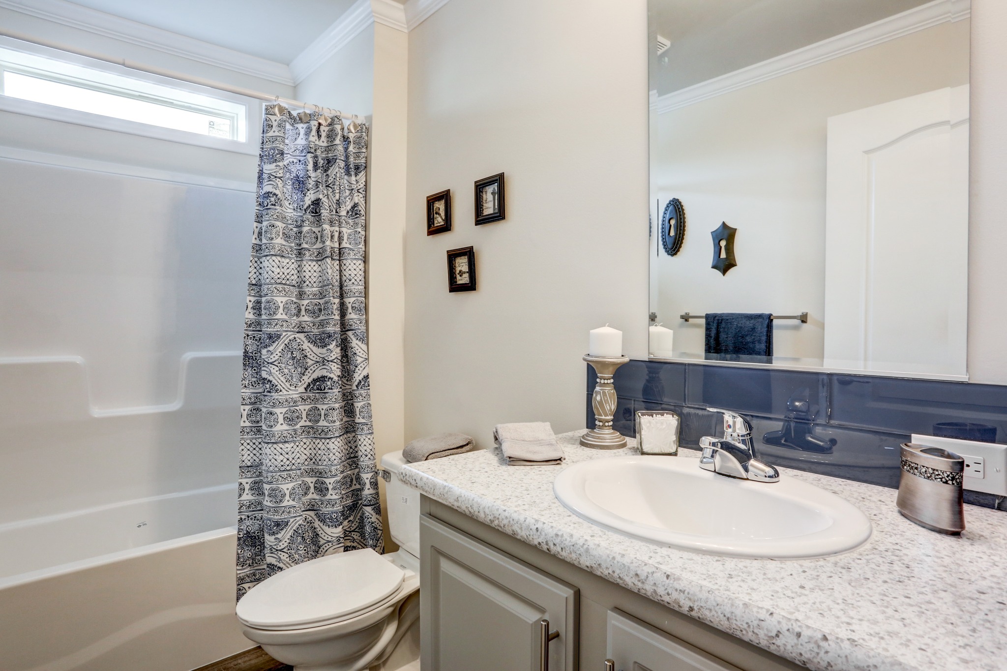 Bright bathroom with a modern design features a patterned shower curtain, granite countertop, white sink, candles, and small framed pictures. Clean and serene ambiance.