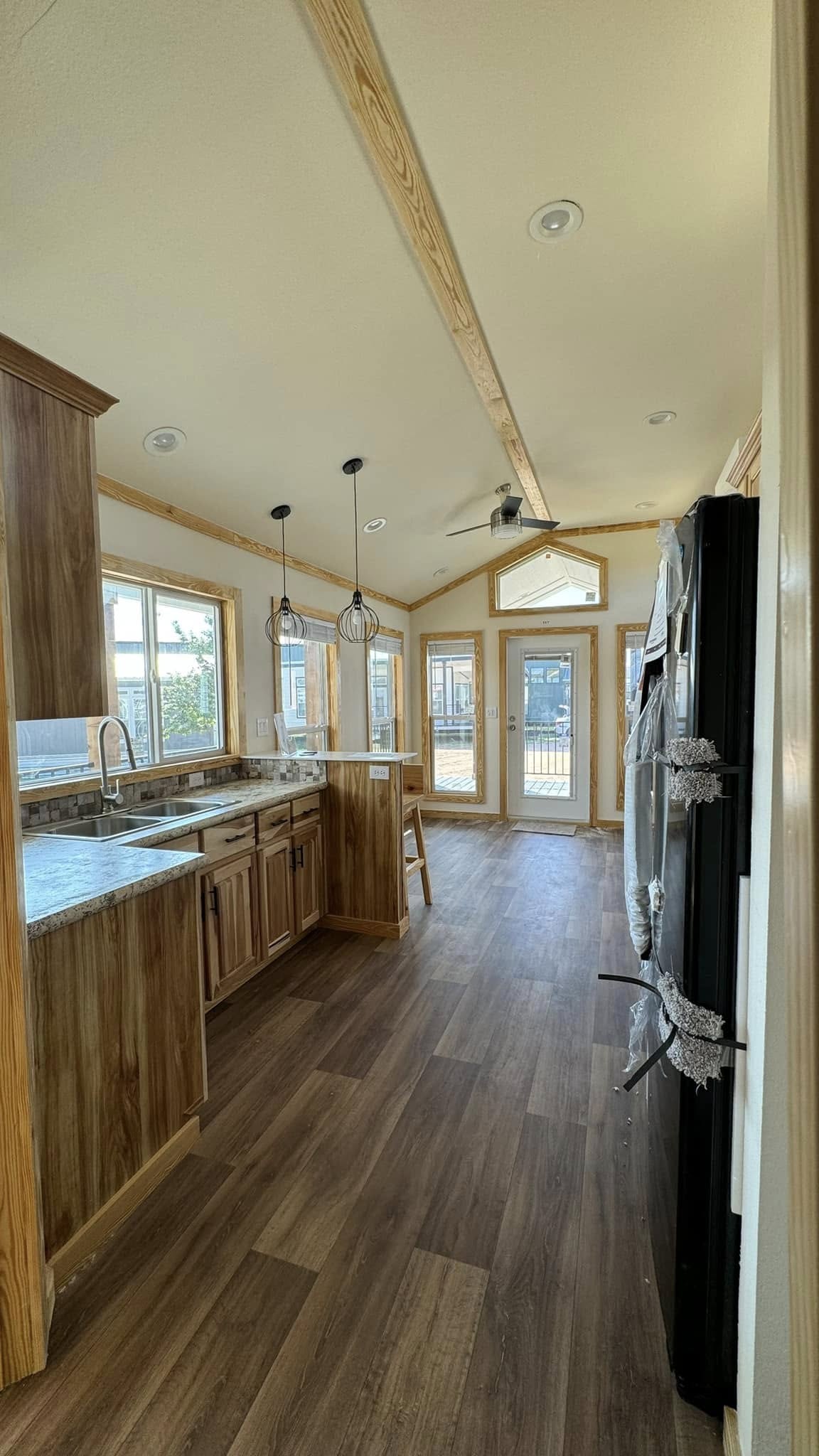 Sleek kitchen interior with wooden cabinets, granite countertops, and large windows. Pendant lights and a ceiling fan add modern flair. Bright and inviting.