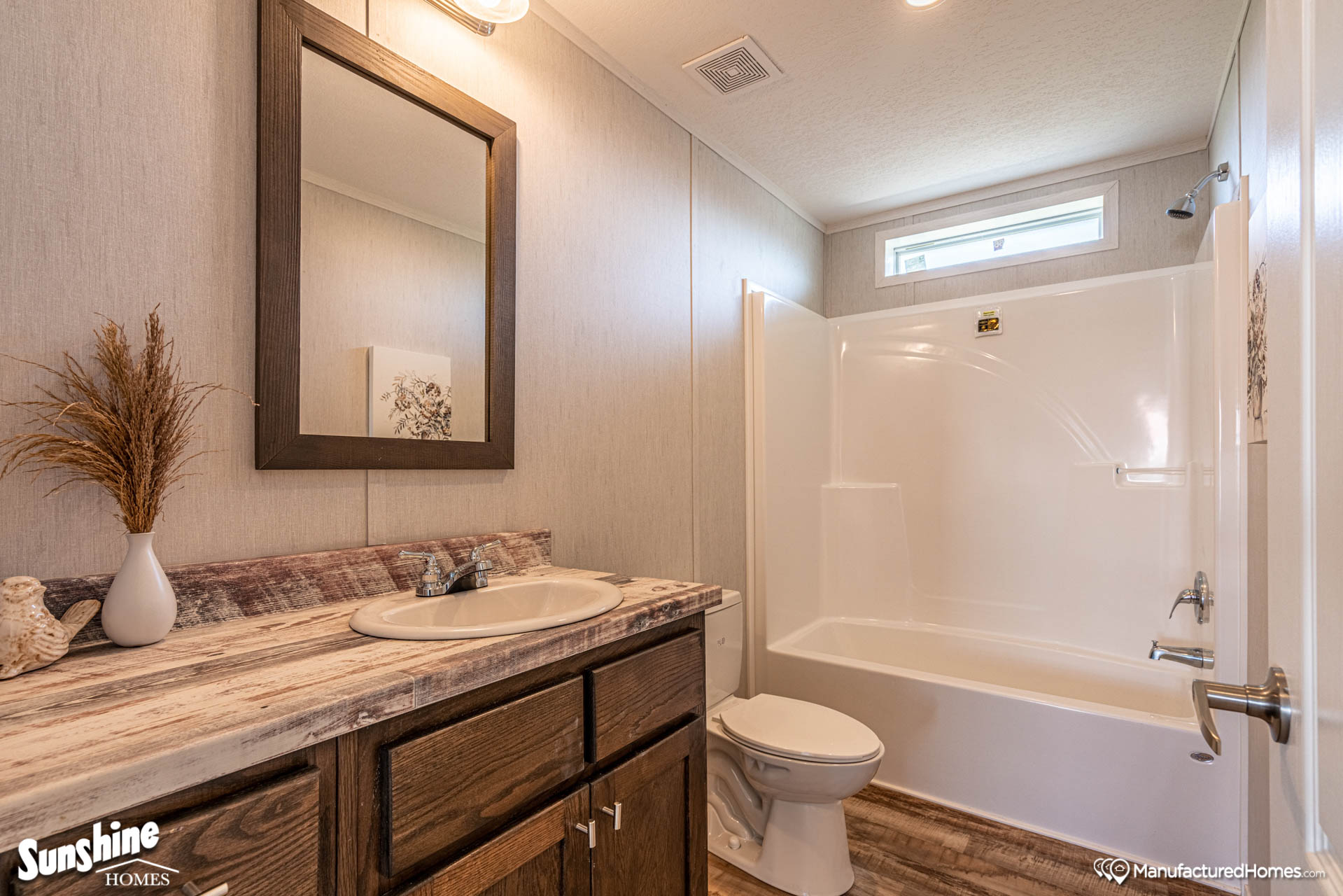 A modern bathroom with a wooden vanity and marble-patterned countertop. It features a large mirror, white bathtub, and decorative plants, creating a cozy and clean atmosphere.