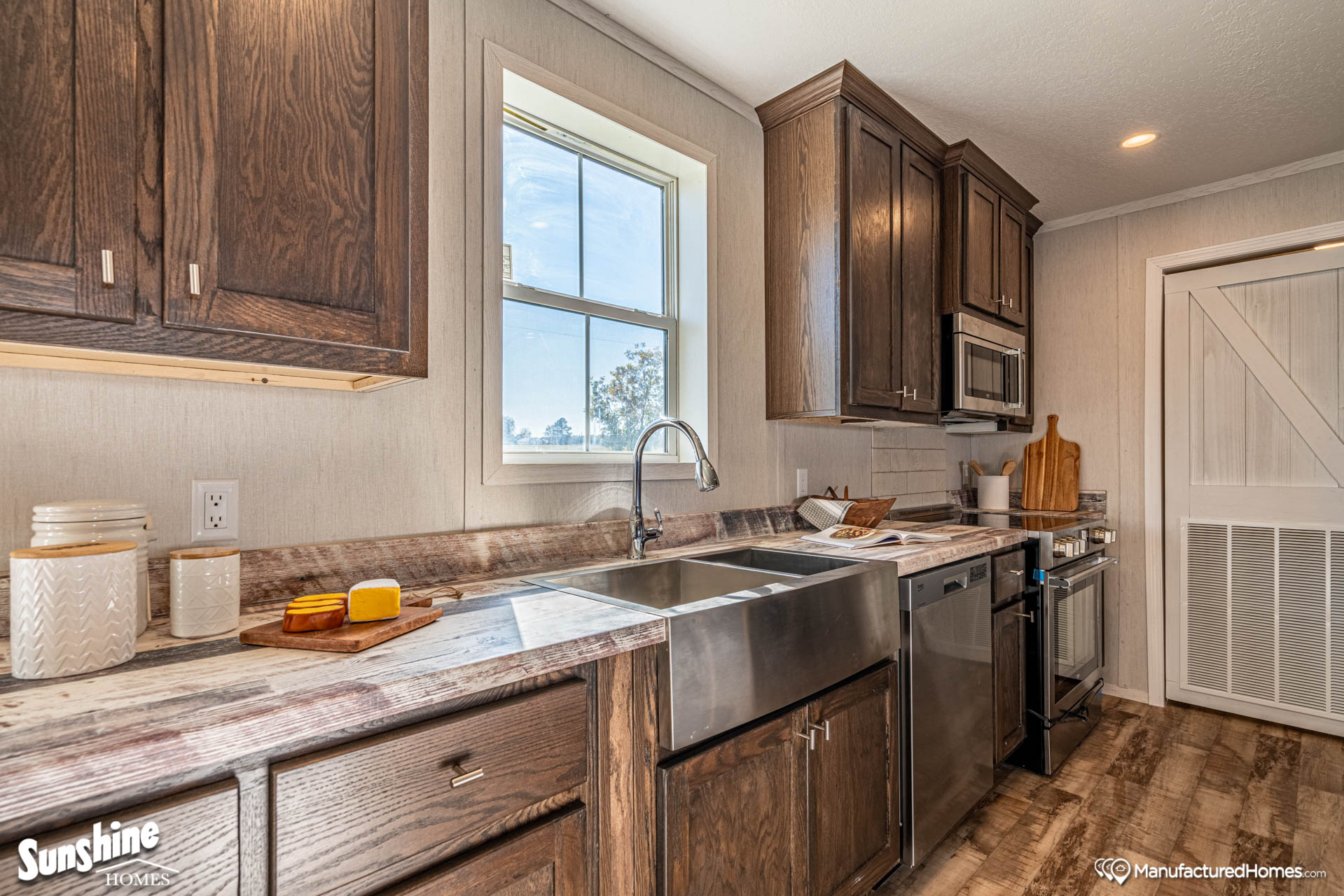 A modern kitchen with rustic charm features dark wooden cabinets and a textured countertop. A stainless steel sink and appliances add sleekness, while ample natural light from a window brightens the space, creating a warm, inviting atmosphere.