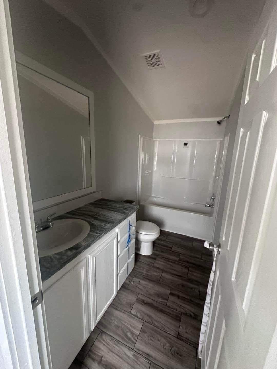 Narrow bathroom with gray tiles, white cabinet and countertop. Features a toilet, bathtub, and a large mirror, creating a clean, minimalistic feel.