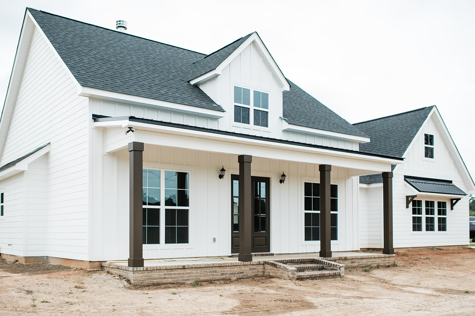 A modern farmhouse with white siding and black roof, featuring large windows and a porch with dark pillars, exudes a clean, welcoming vibe.
