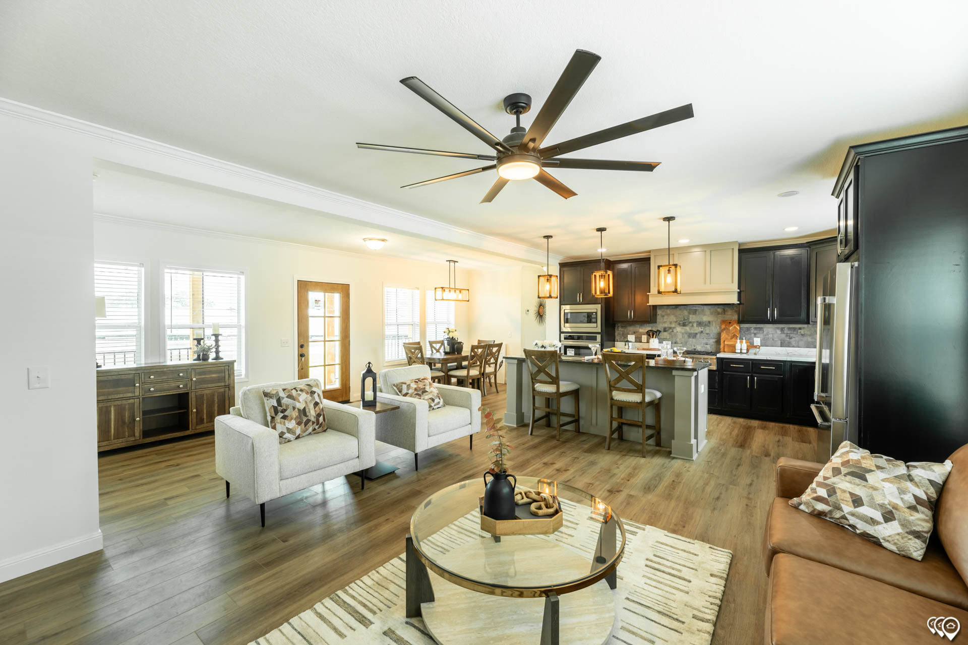Bright, modern open-concept living room and kitchen with wood floors. Features a ceiling fan, beige furniture, island, and pendant lighting. Cozy and inviting.