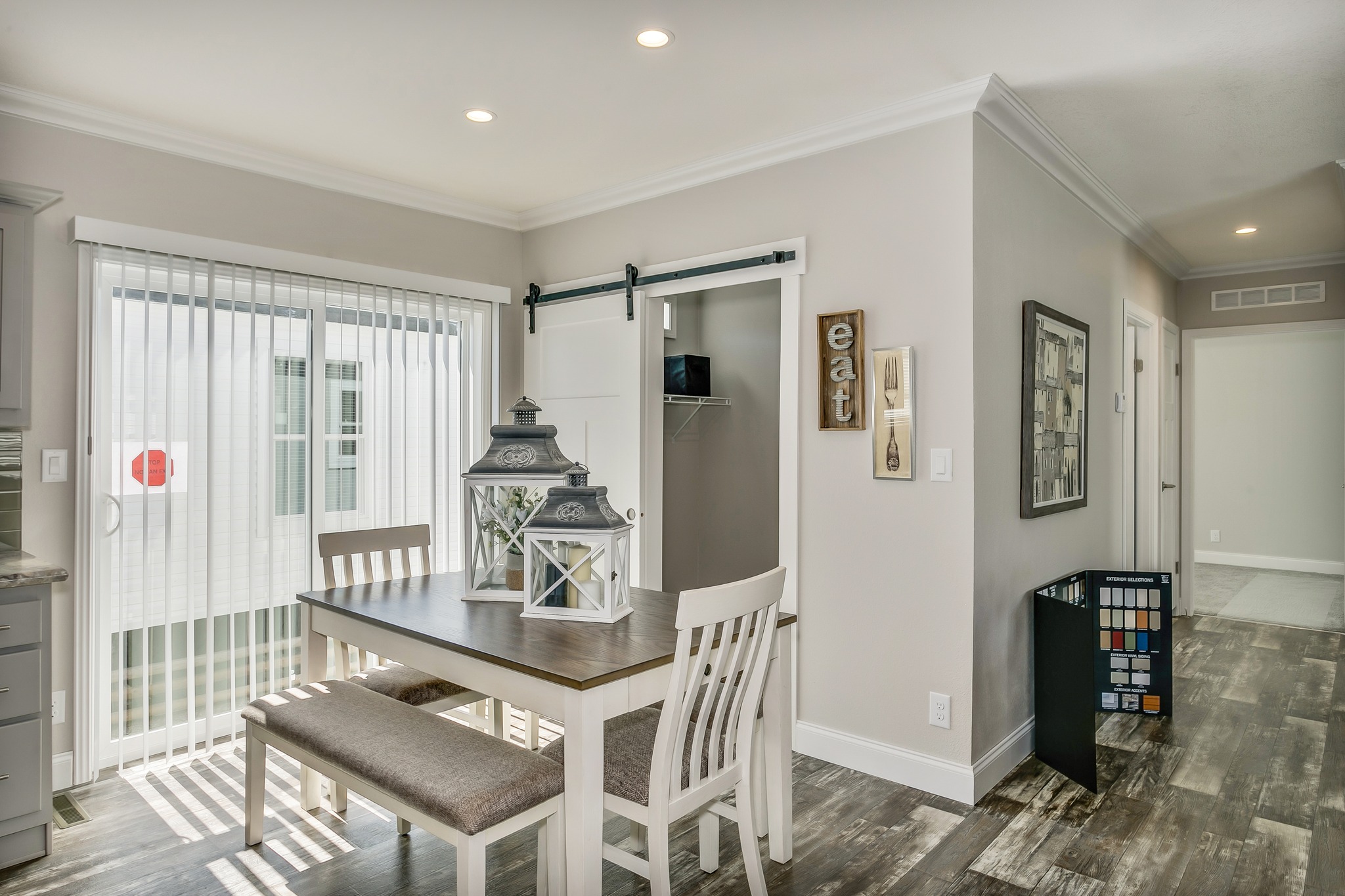 Bright dining area with a wooden table, white chairs, and decorative lanterns. Sliding glass door with blinds, barn door, neutral tones, cozy ambiance.