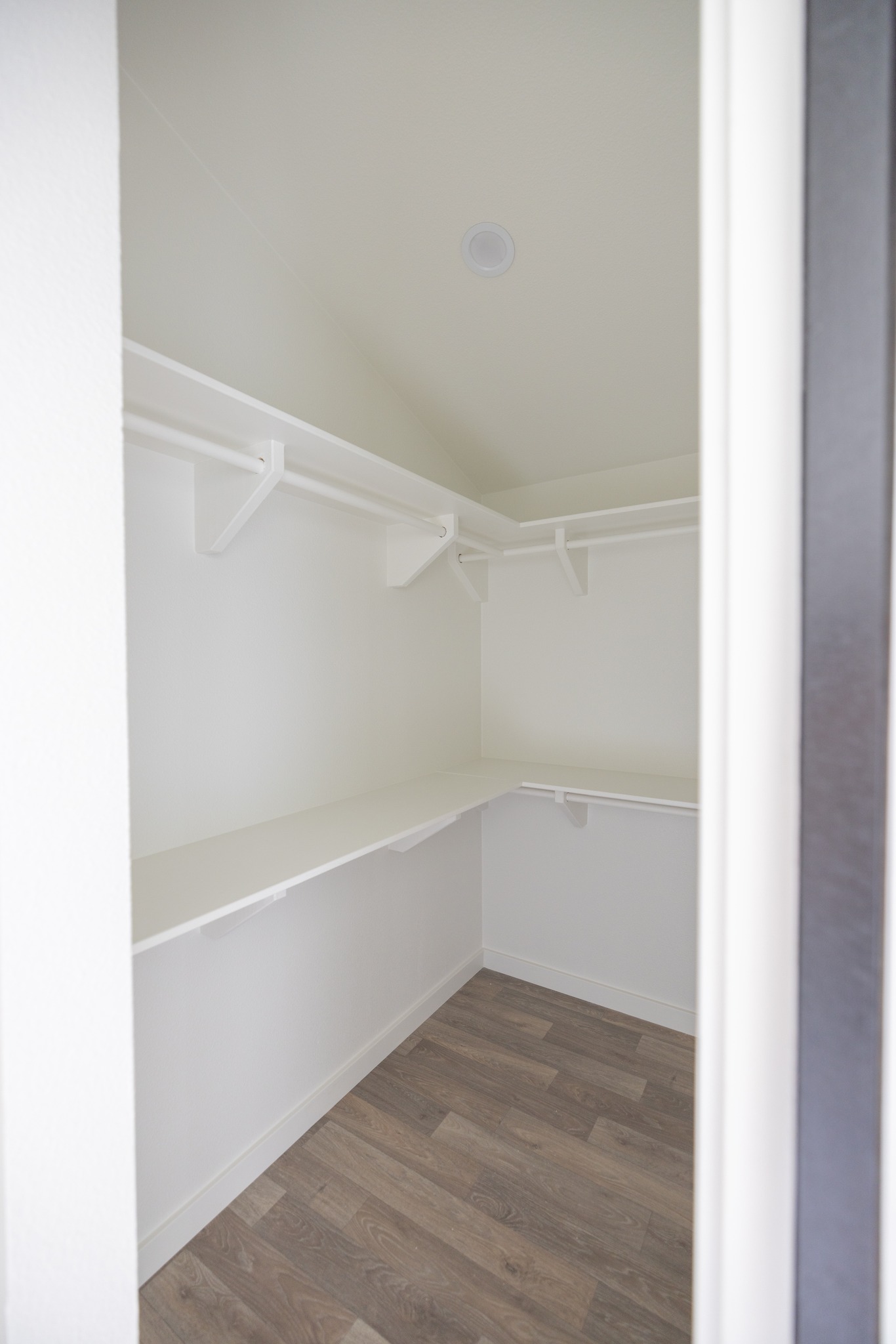 Walk-in closet with white walls, wooden flooring, and empty shelves on both sides. The space is bright and minimalist, conveying a clean, organized feel.