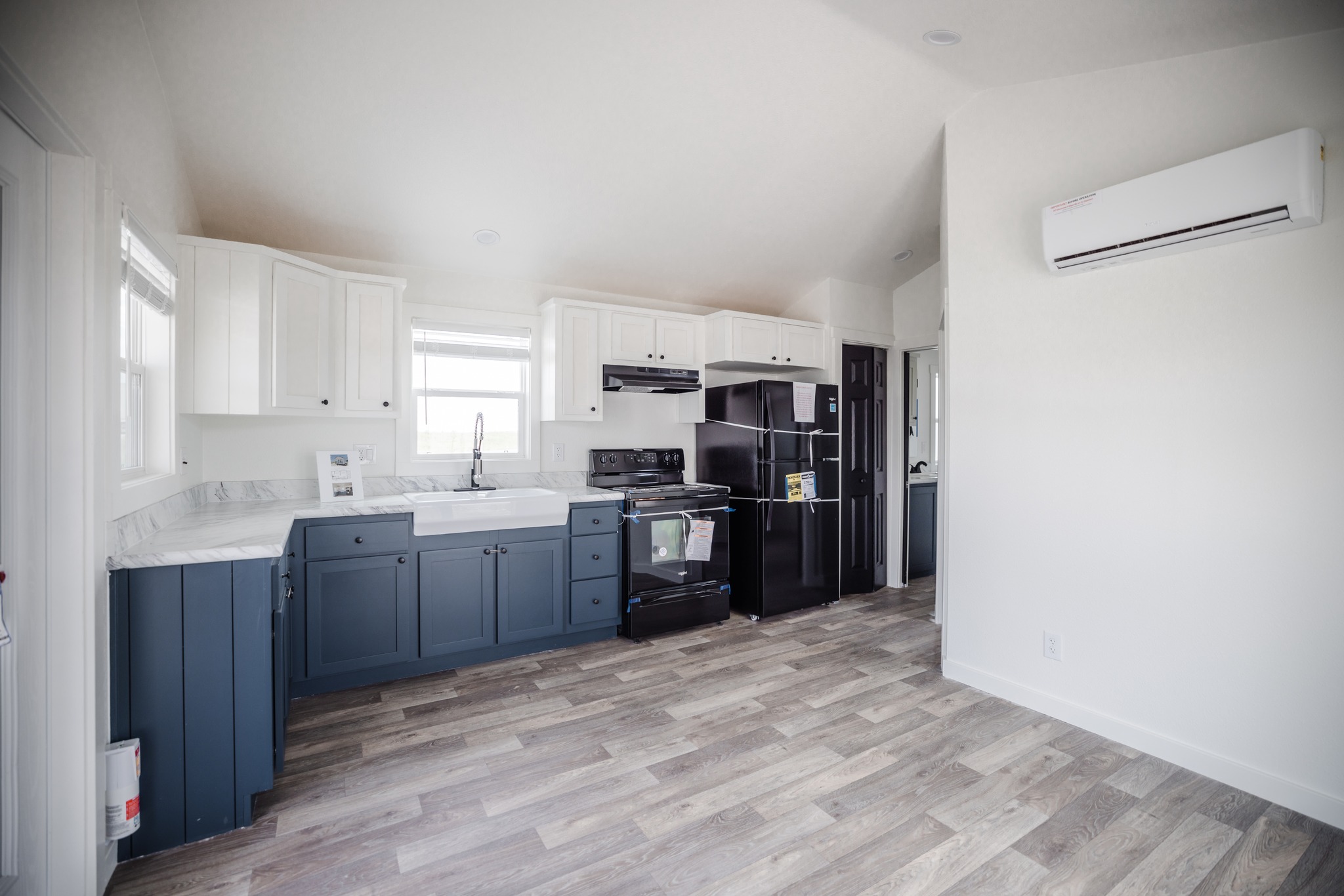 Modern kitchen with navy and white cabinets, black appliances, and a farmhouse sink. Light wood flooring enhances the spacious, clean atmosphere.