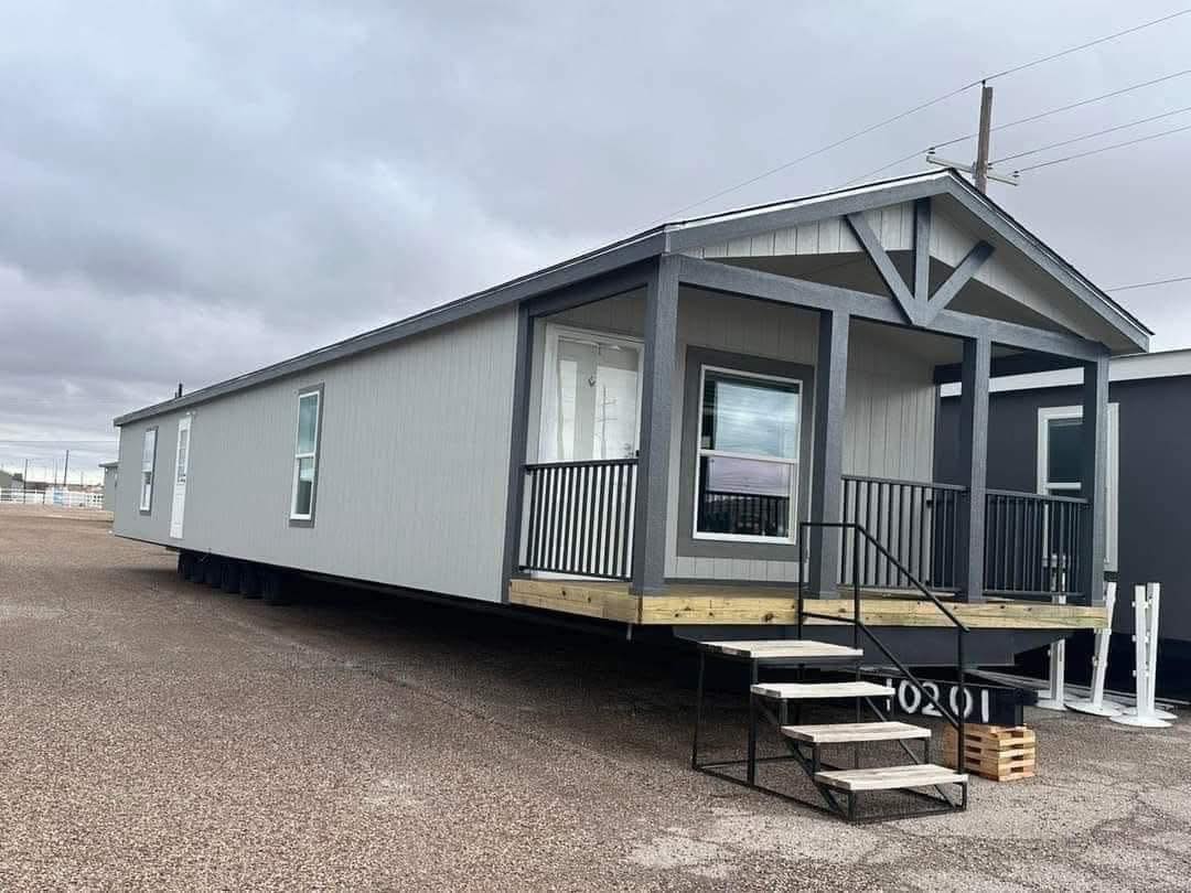 Gray modular home with gabled roof, small porch, and stairs. The setting is overcast, suggesting a calm and practical atmosphere.