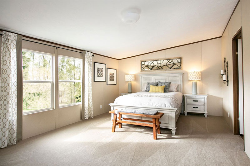 Bright bedroom with a large window, white bed and headboard, wooden bench, and matching nightstands. Soft beige tones create a serene, cozy ambiance.