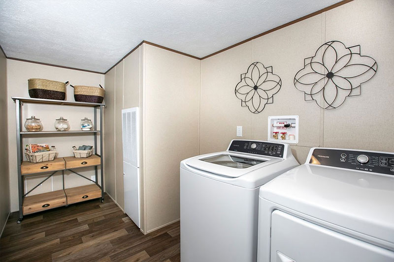 A well-organized laundry room with a washer and dryer. Open shelving holds baskets and jars. Decorative wall art adds a modern touch.