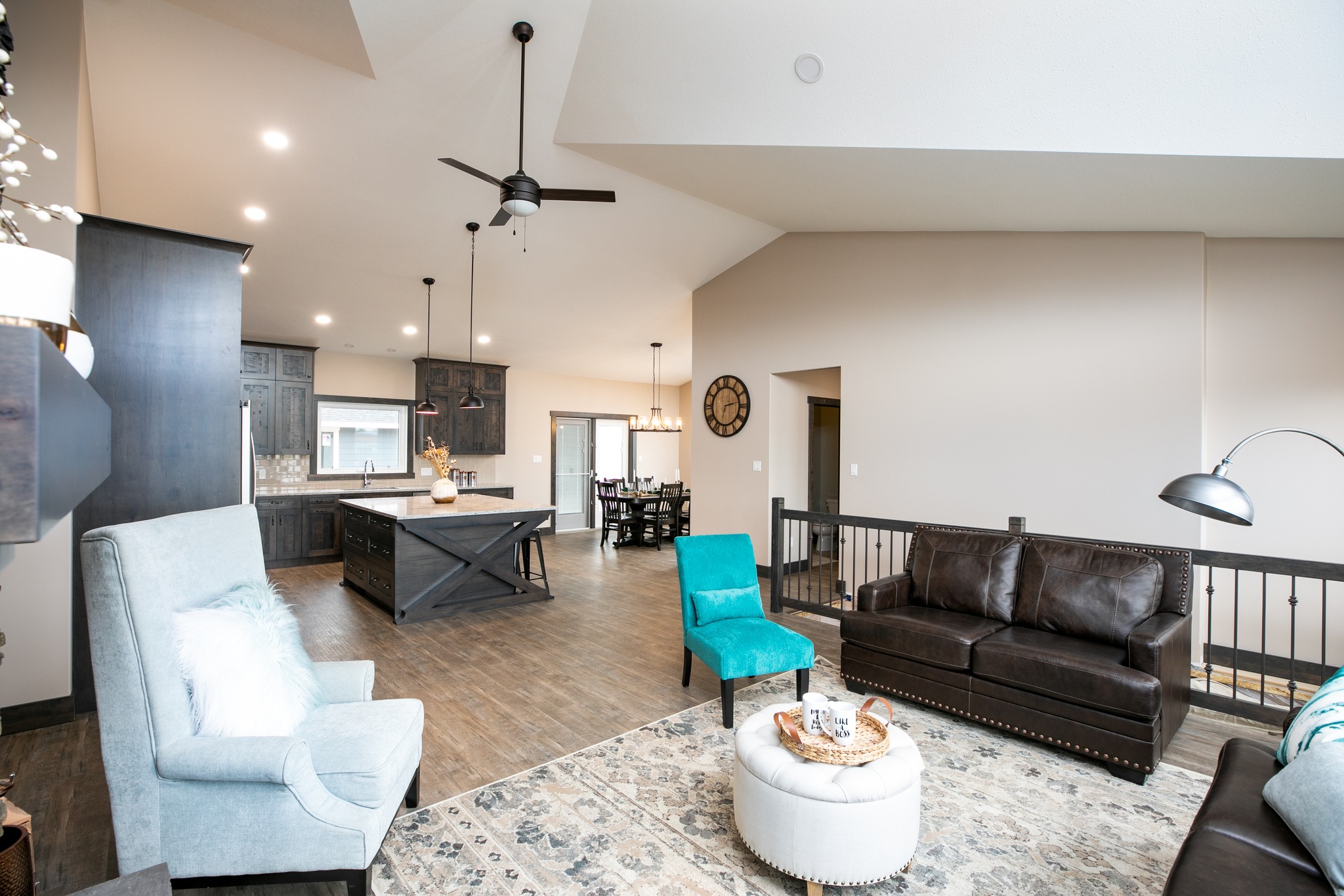 Modern living room with high ceilings, featuring a black leather sofa and light blue armchair. Open kitchen with dark cabinets in the background. Cozy ambiance.