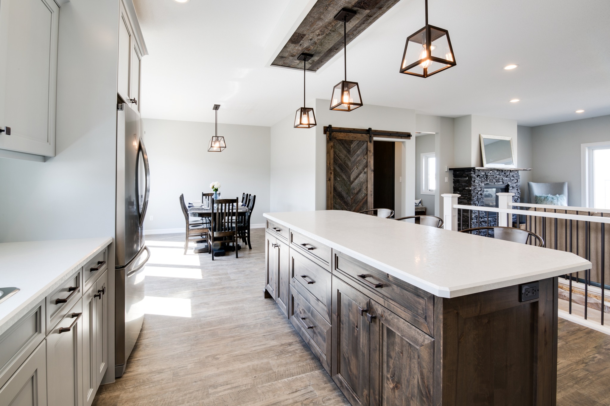 Spacious modern kitchen with a large island featuring wooden cabinets and white countertop. Pendant lights hang above, and a barn door is visible.