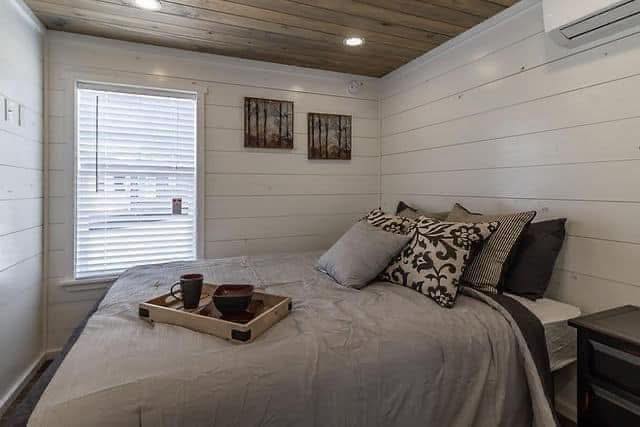 Cozy bedroom with wood-paneled walls and ceiling, a bed with patterned pillows, and a tray with mugs. Calm, inviting atmosphere with soft lighting.