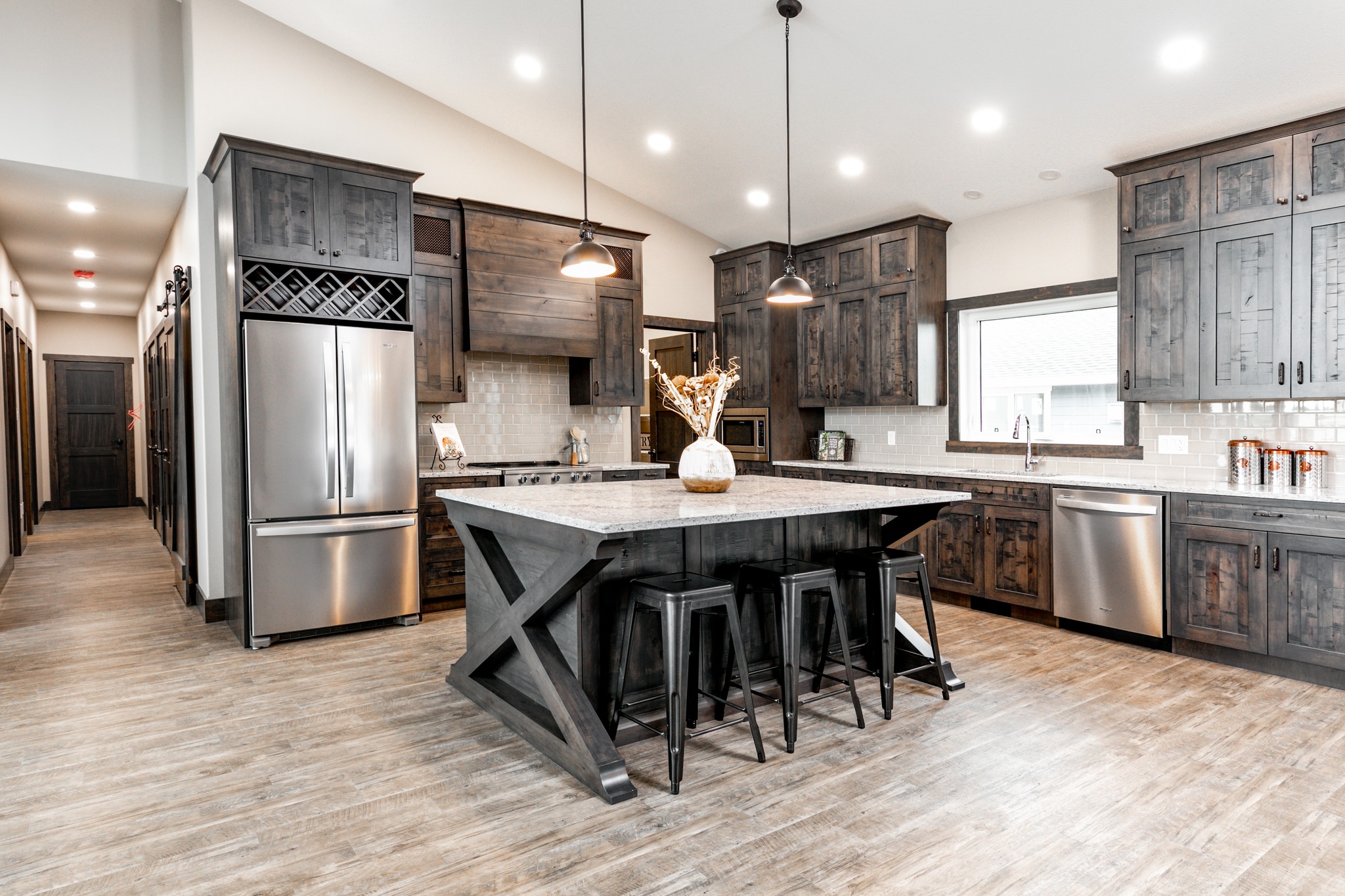 Modern kitchen with dark wood cabinets, a large island with black stools, stainless steel appliances, and pendant lights. Rustic yet elegant ambiance.