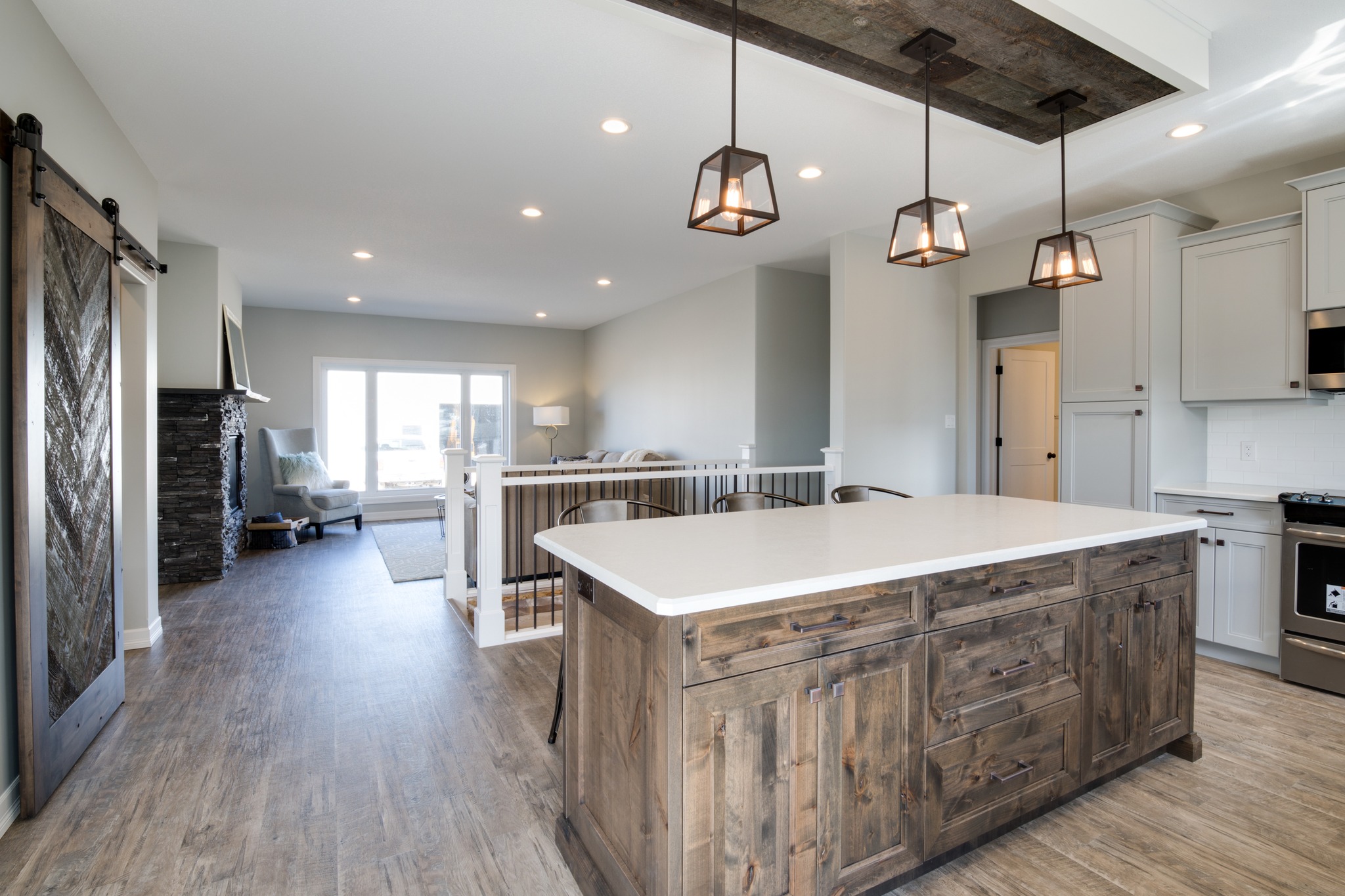 Modern open-concept kitchen and living area with a rustic wood island, pendant lights, and sliding barn door. Bright, inviting atmosphere.