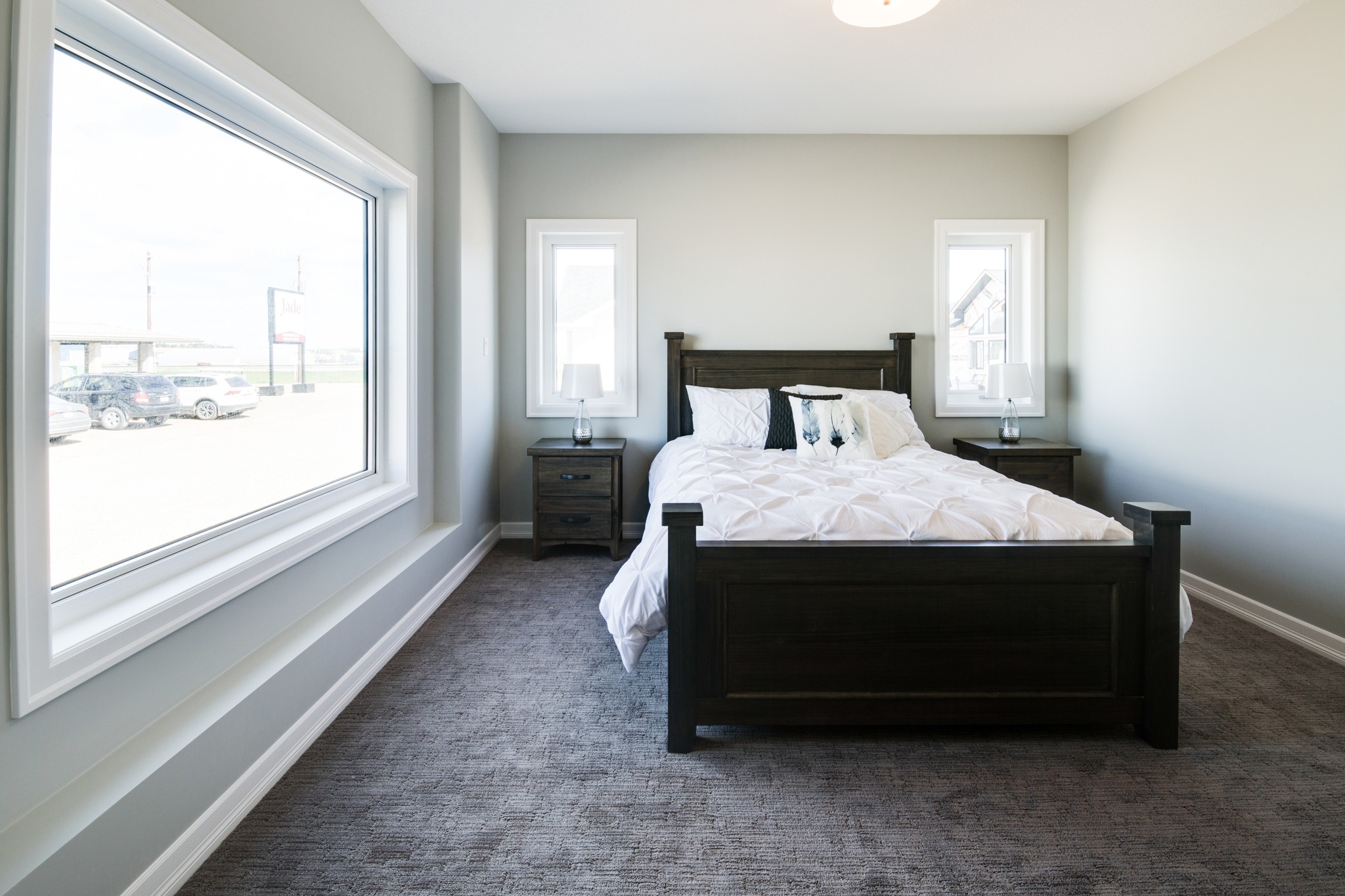 Bright bedroom with a large window on the left, gray walls, and a dark wooden bed. Two bedside tables with lamps flank the bed, creating a serene atmosphere.