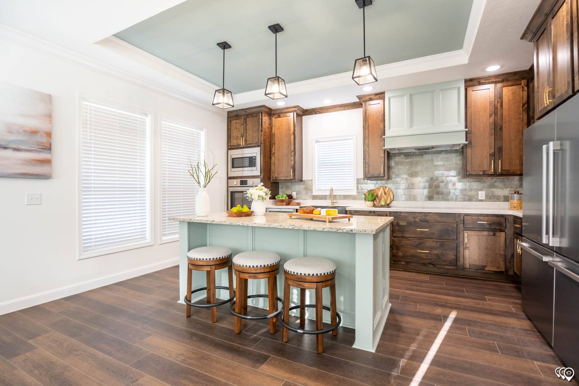 Bright kitchen with a large island featuring turquoise accents and wooden stools. Dark wood cabinets, modern appliances, and pendant lights add warmth.