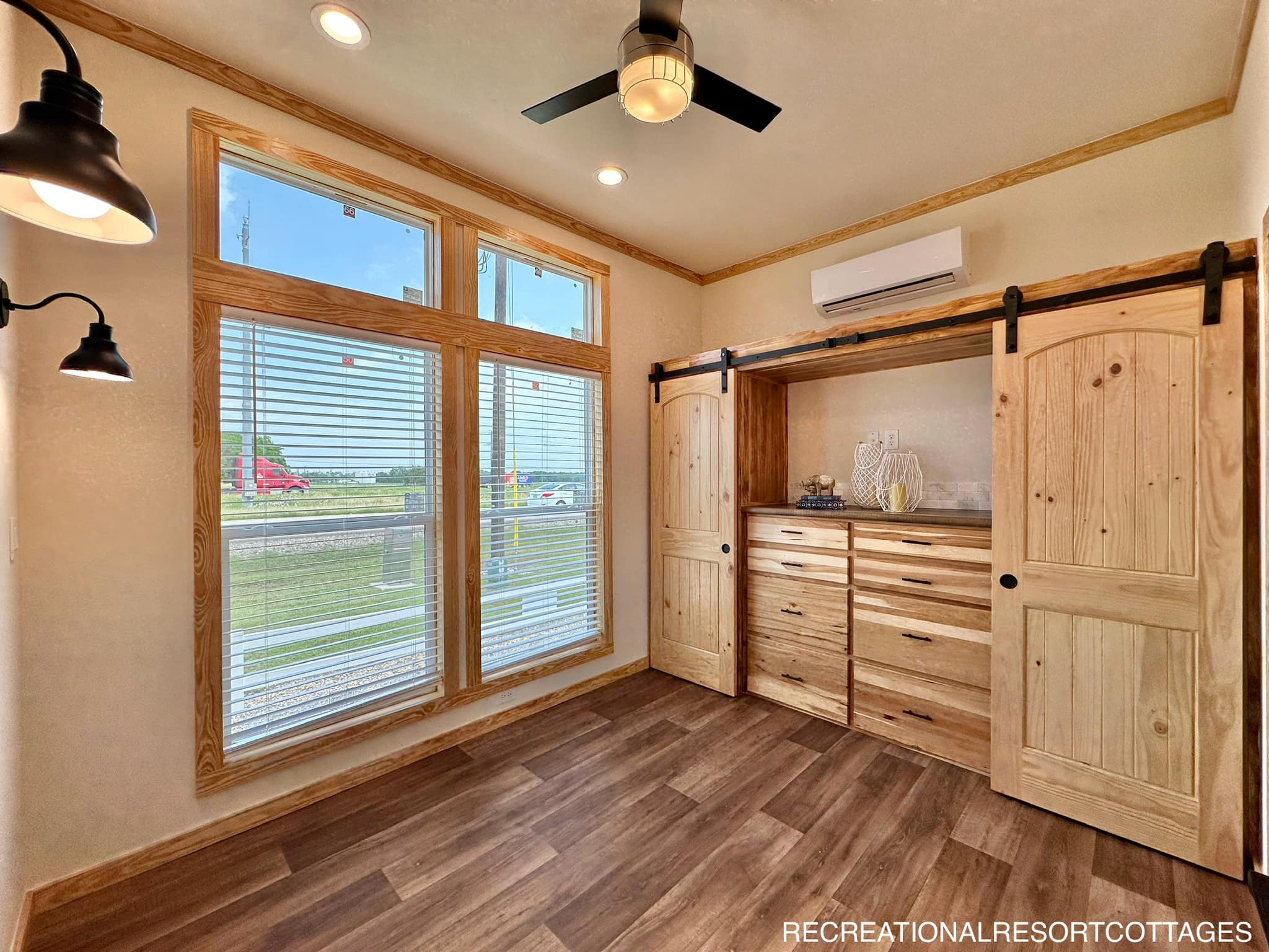 Cozy room with large windows, wooden floors, and a ceiling fan. Features a built-in cabinet with sliding barn doors. Bright and inviting atmosphere.
